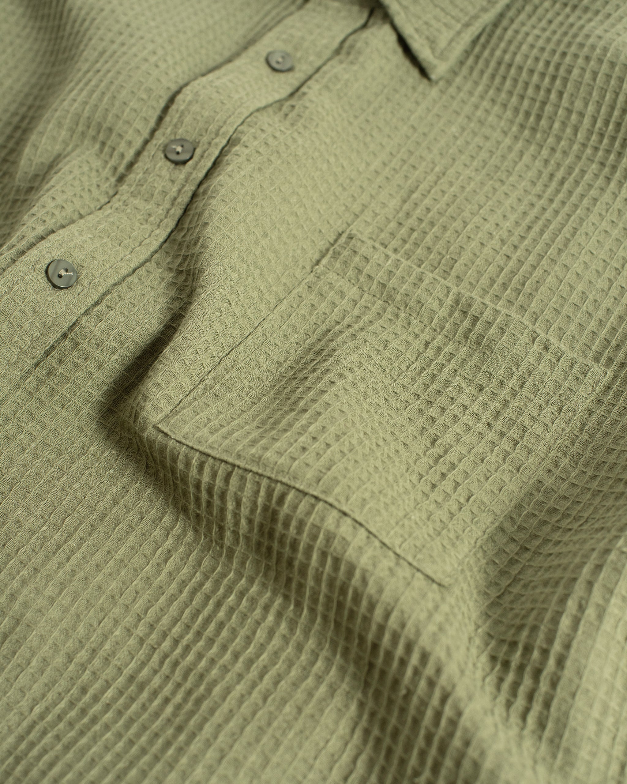 A close-up detail of the Bather Men's Artichoke Waffle Leisure Shirt, highlighting the textured olive green cotton-linen waffle weave fabric, the chest pocket, and the tonal button placket.