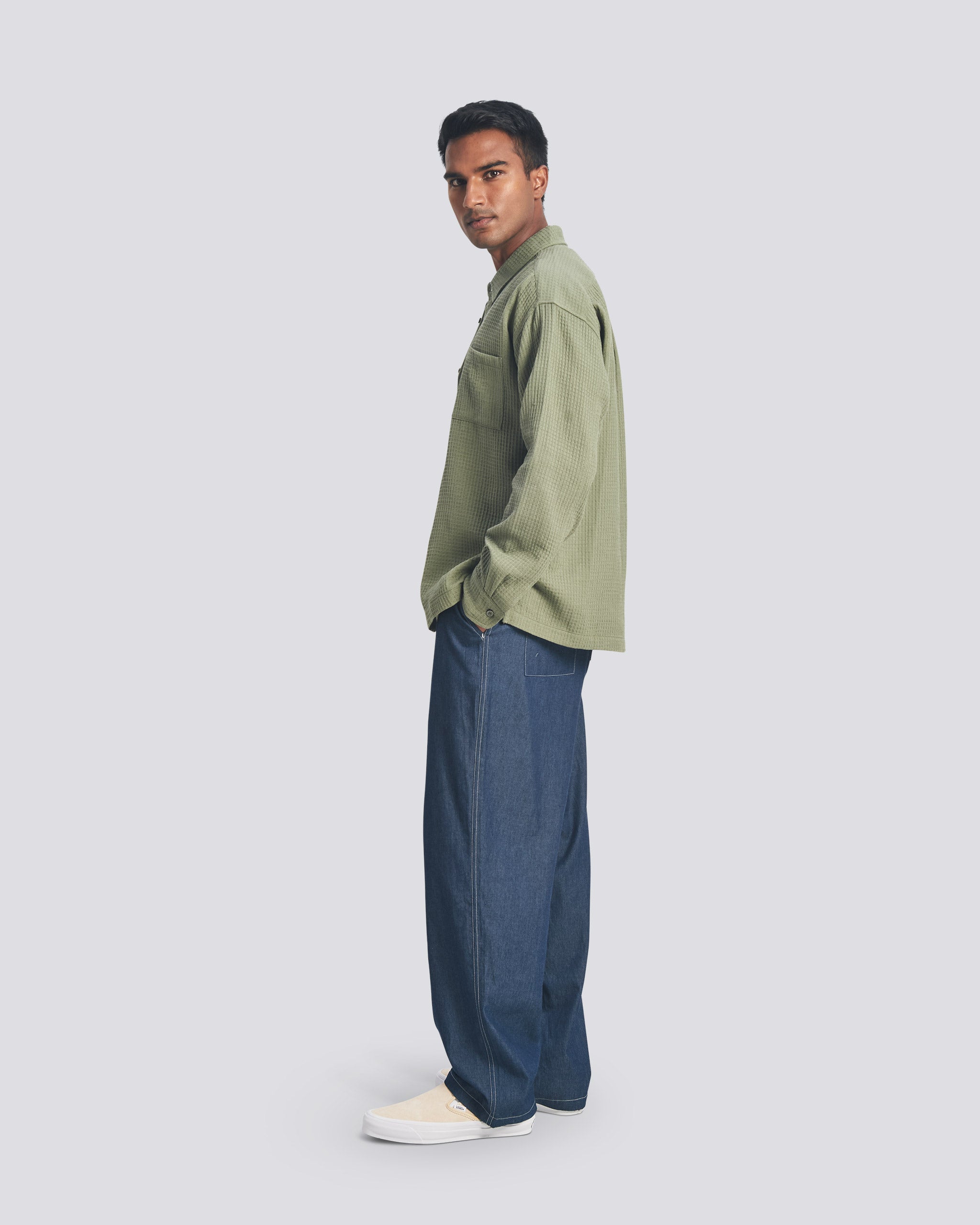Side profile of a model wearing the Bather Men's Artichoke Waffle Leisure Shirt, showcasing the oversized fit and long-sleeve silhouette paired with dark navy trousers and cream slip-on shoes.