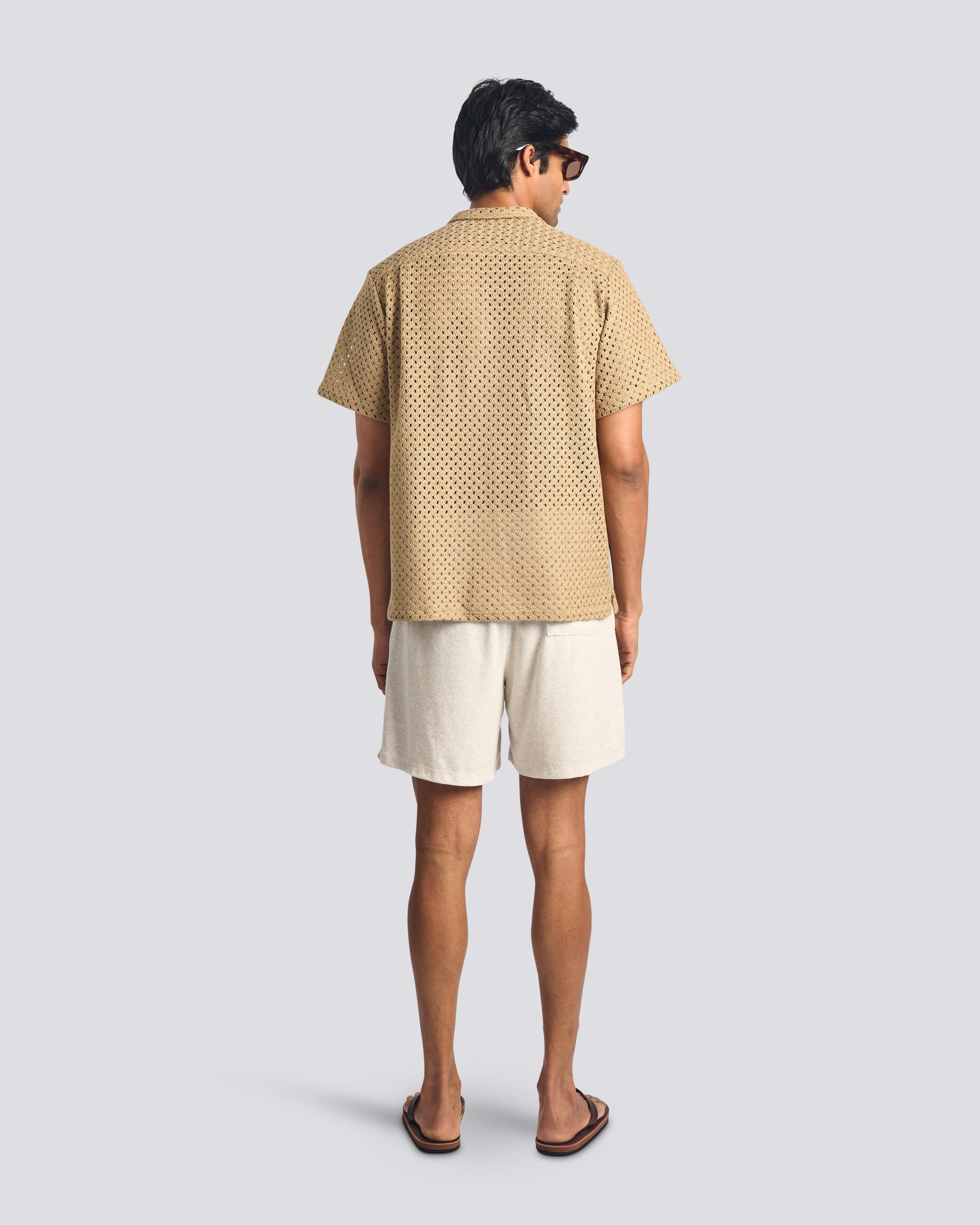 Back view of a model wearing the Bather Men's Beach Mesh Traveler Shirt, showcasing the natural-colored Japanese cotton crocheted mesh fabric and the relaxed, straight-hem silhouette.