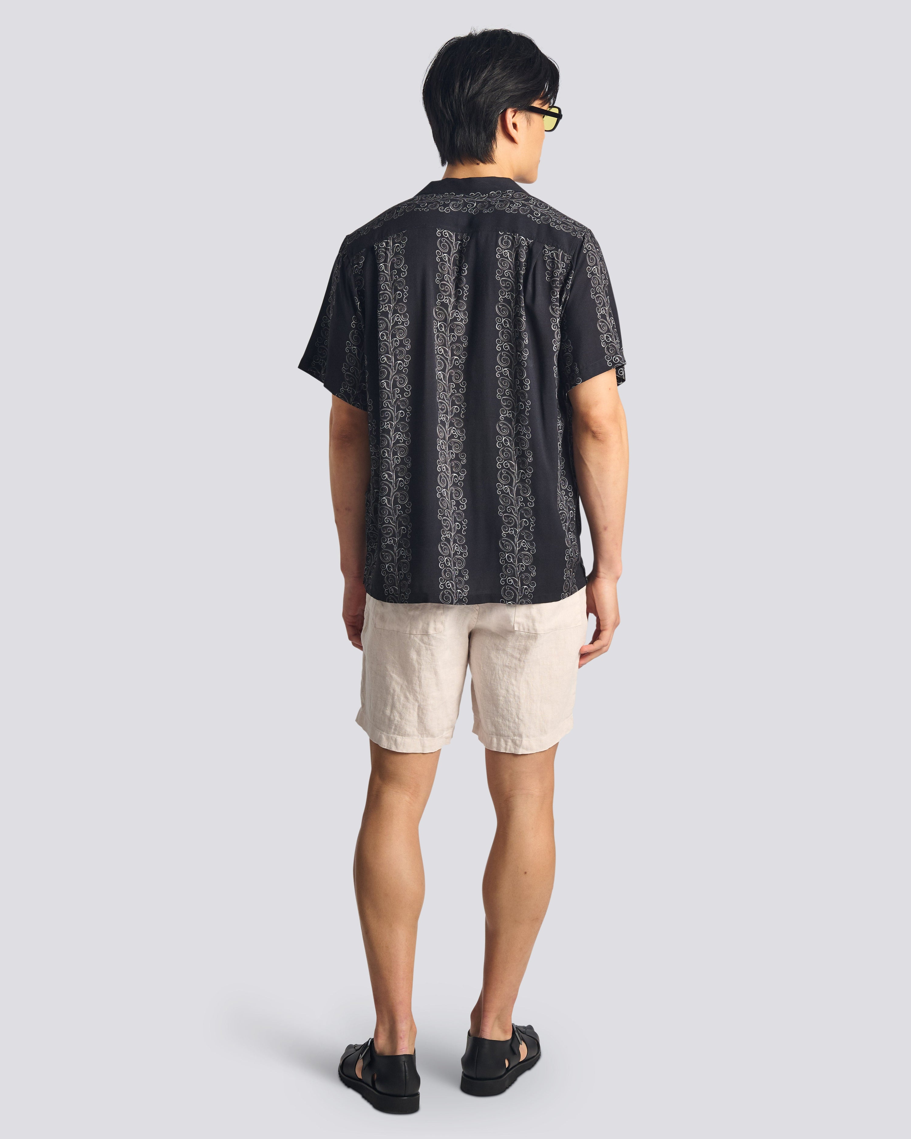 Back view of a model wearing the Bather Men's Black Fiesta Camp Shirt, highlighting the relaxed fit and the lightweight black rayon fabric with a subtle vertical "Fiesta" stripe pattern.