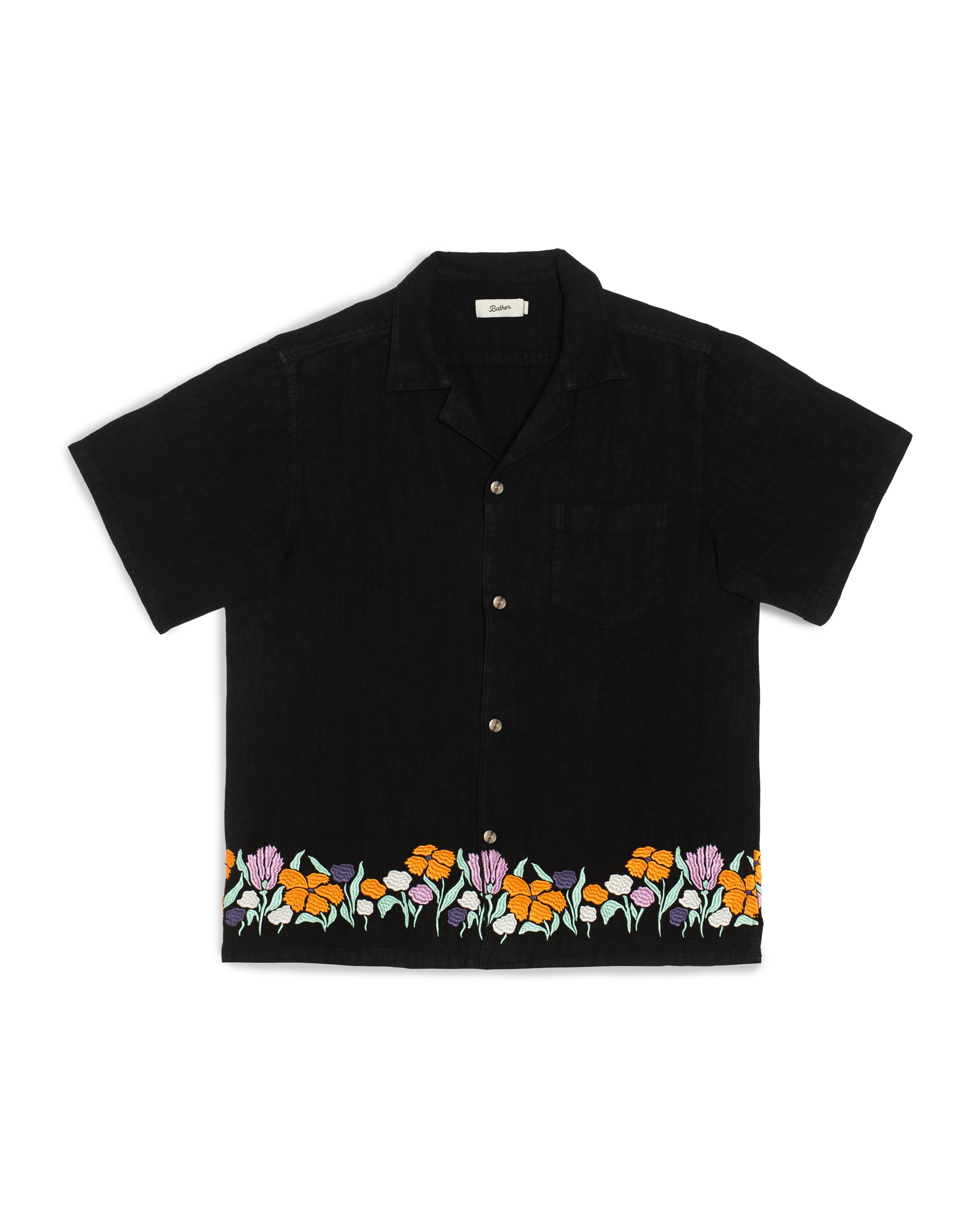 Front view of the Bather Men's Black Lawn Linen Camp Shirt, featuring a black linen fabric with a vibrant floral embroidery along the hem in shades of orange, purple, and white, a single chest pocket, and a classic open camp collar against a white background.