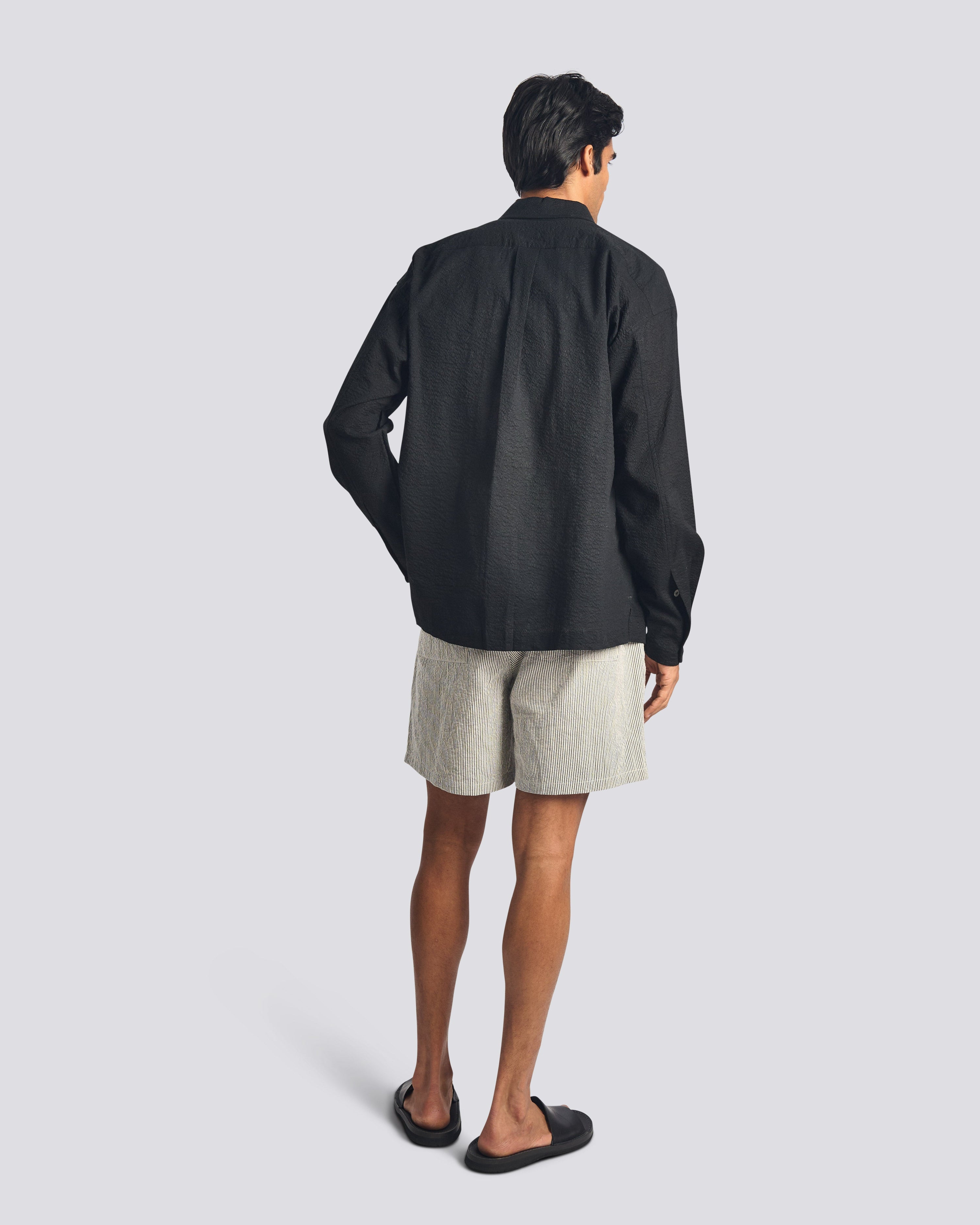 Back view of a model wearing the Bather Men's Black Ripple Leisure Shirt, highlighting the relaxed, straight-hem silhouette and the subtle seersucker texture of the black Japanese cotton fabric.