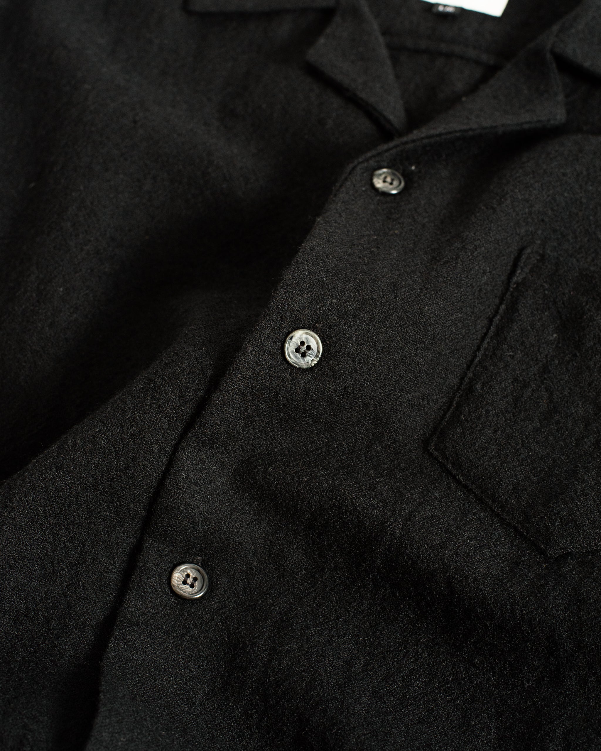 A close-up detail of the Bather Men's Black Wool Gauze Camp Shirt, showcasing the fine texture of the 100% Japanese worsted wool gauze fabric and the contrasting marbled grey buttons.