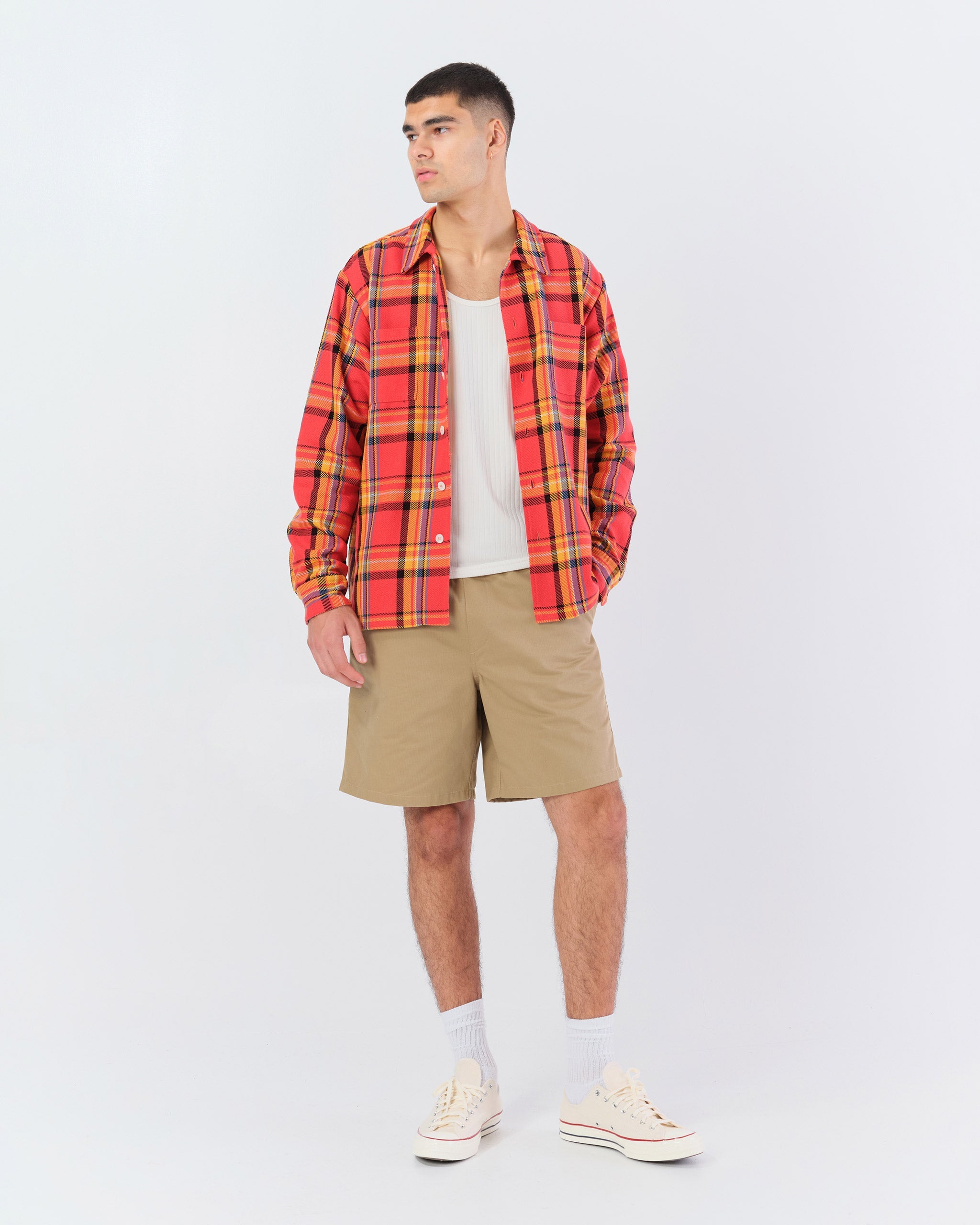 Male model wearing the red Bather Men's Buoy Plaid Flannel overshirt with a closed collar and two chest pockets.