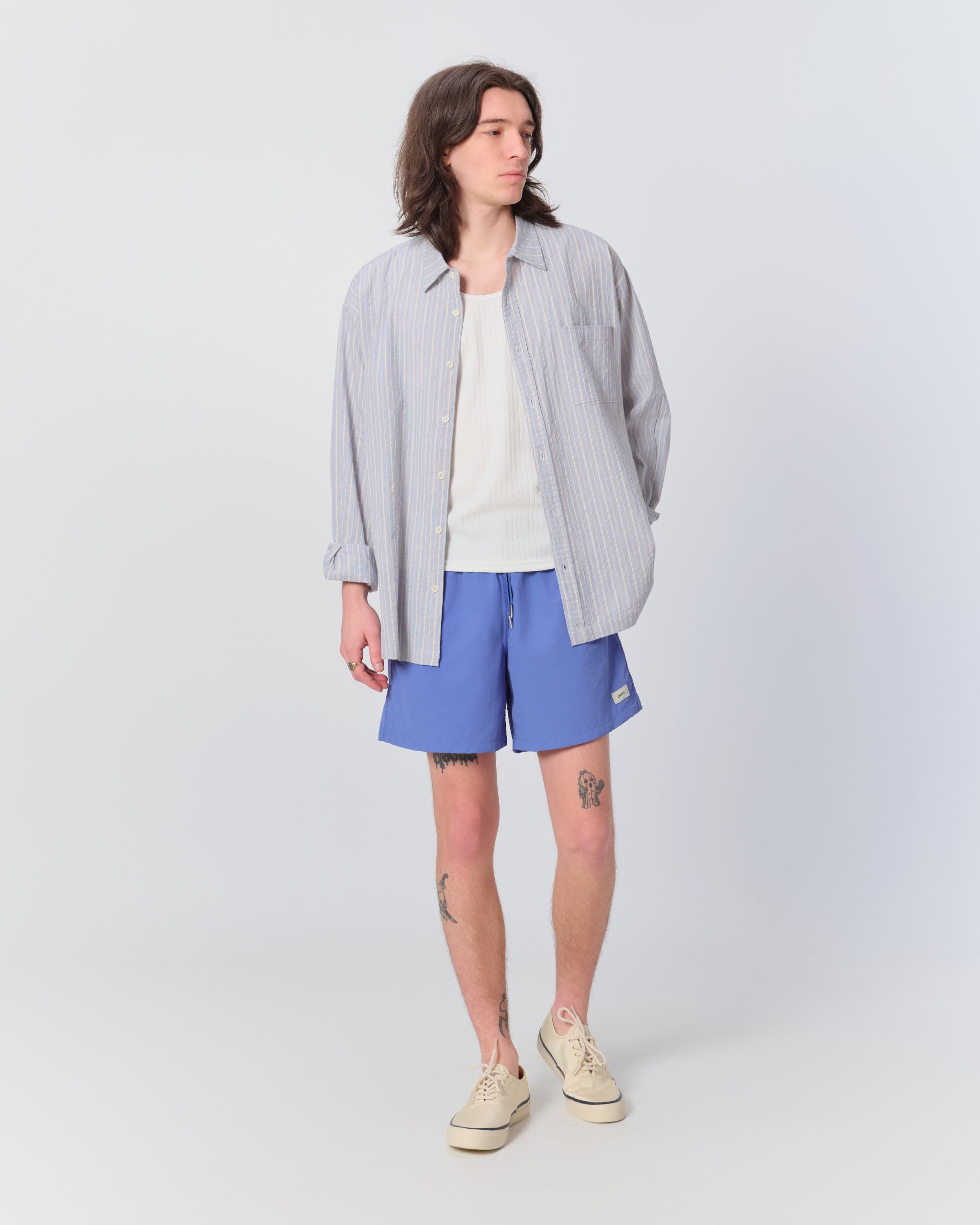 Male model wearing striped button-up long-sleeve shirt with blue swim trunks