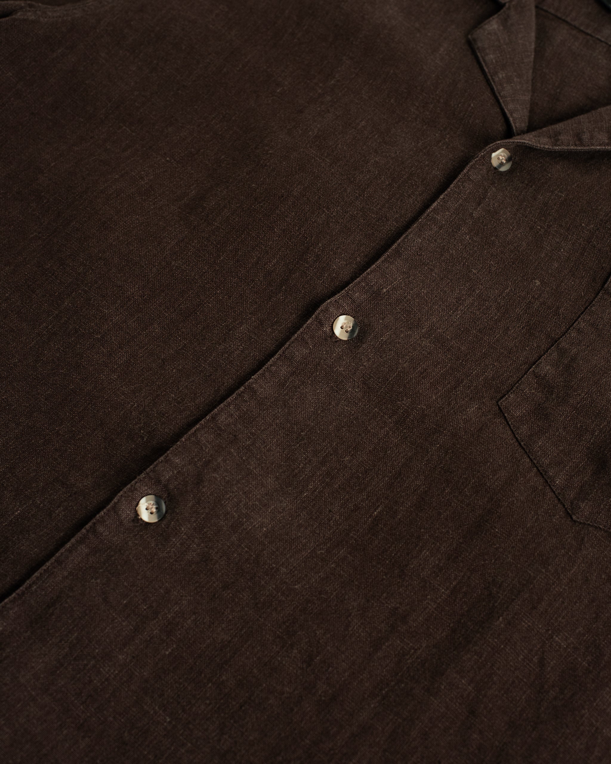 Detailed close-up of the Bather Men's Espresso Linen Camp Shirt highlighting the natural slub texture of the premium dark brown linen fabric.