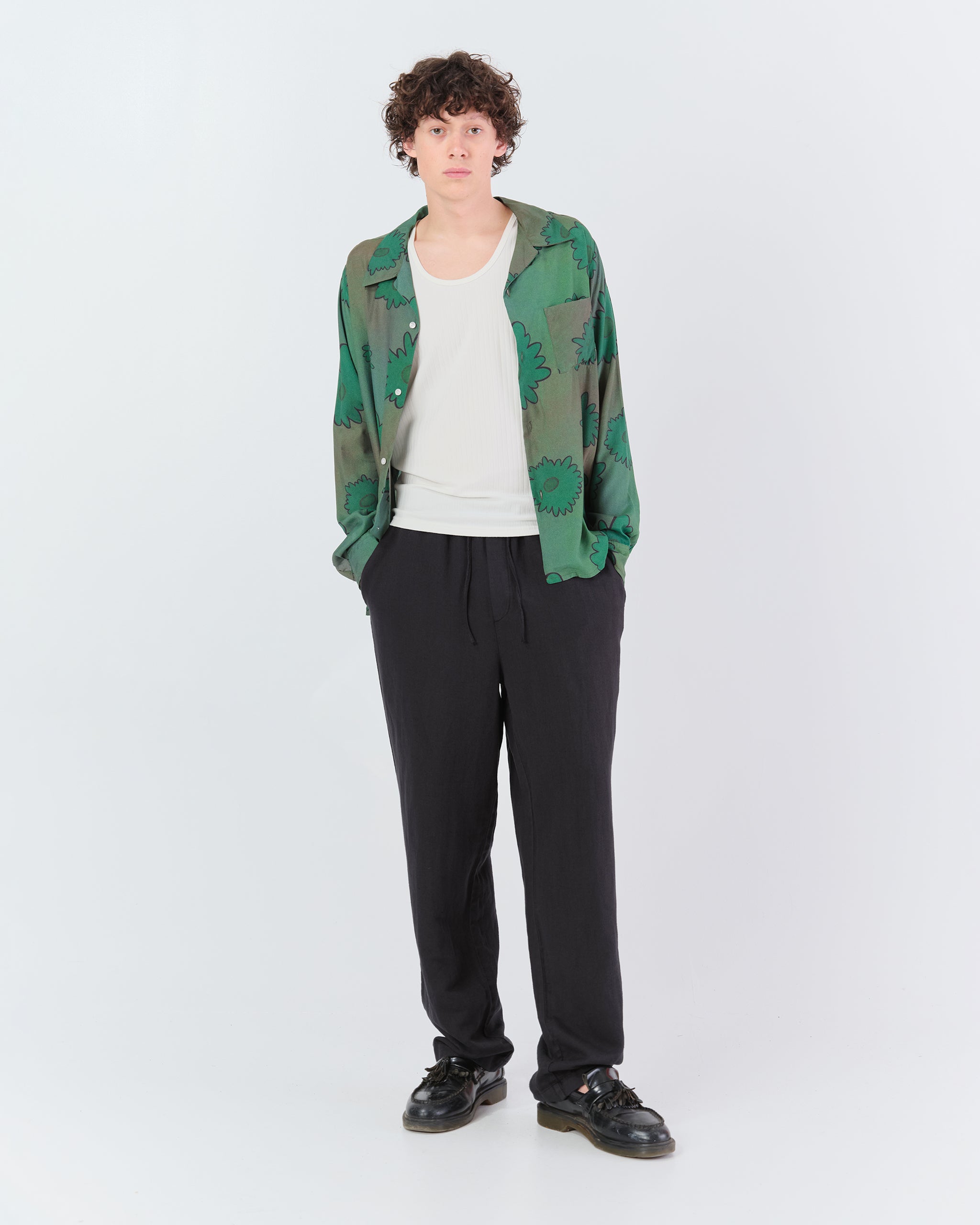 Full-length view of a model wearing the Bather Men's long-sleeve green floral camp shirt and black pants.