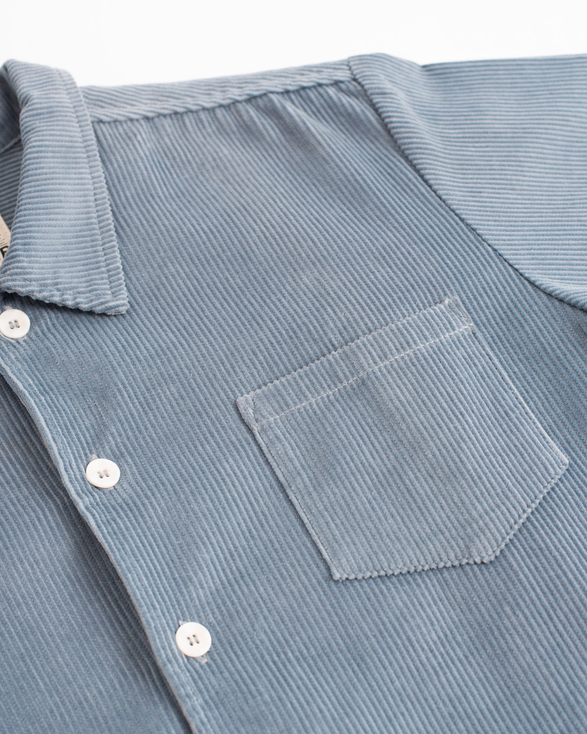 Detailed fabric view of the Bather Men's light blue corduroy shirt with pocket and button details.