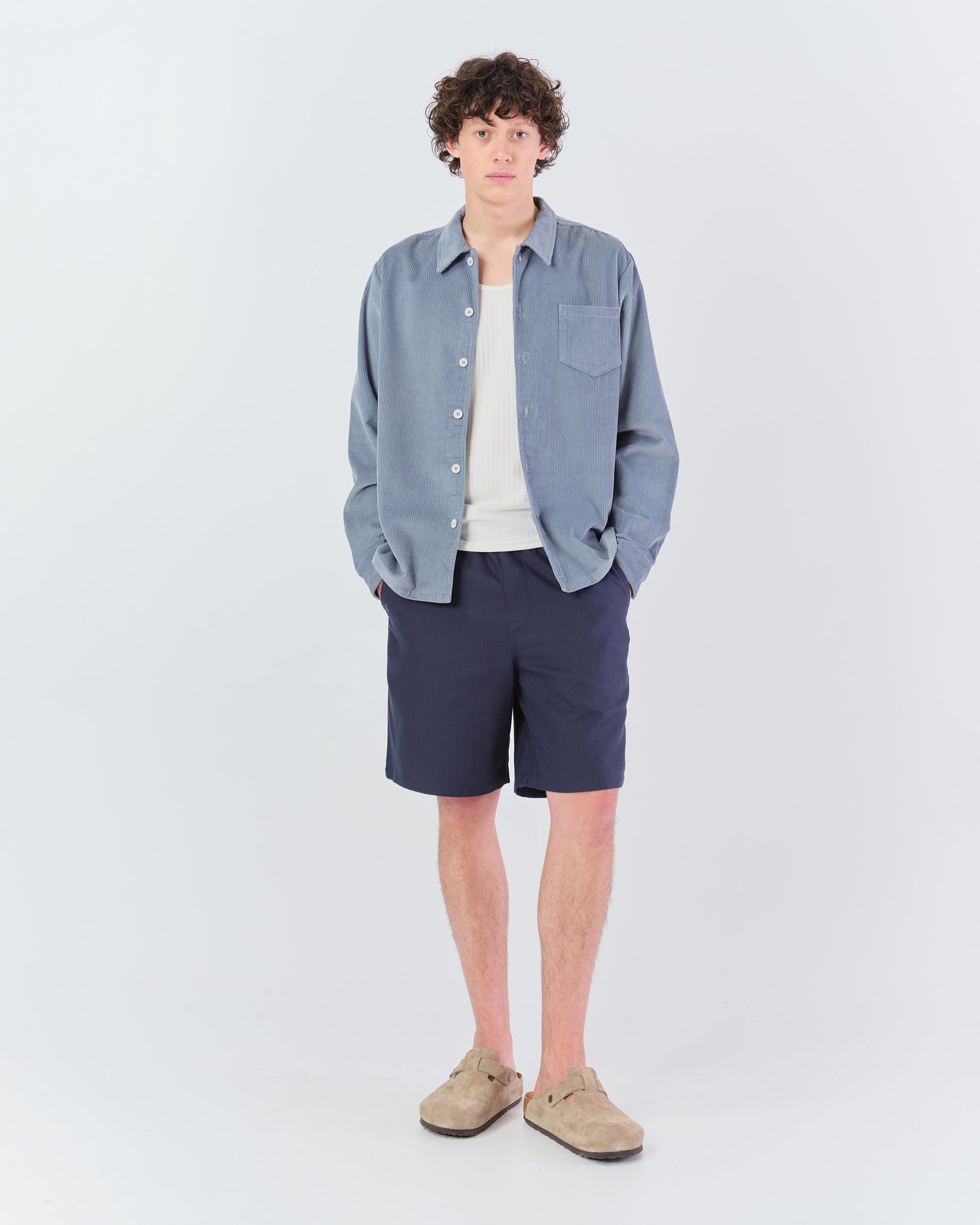 Full-body shot of a model wearing the Bather Men's light blue corduroy shirt styled open with shorts.