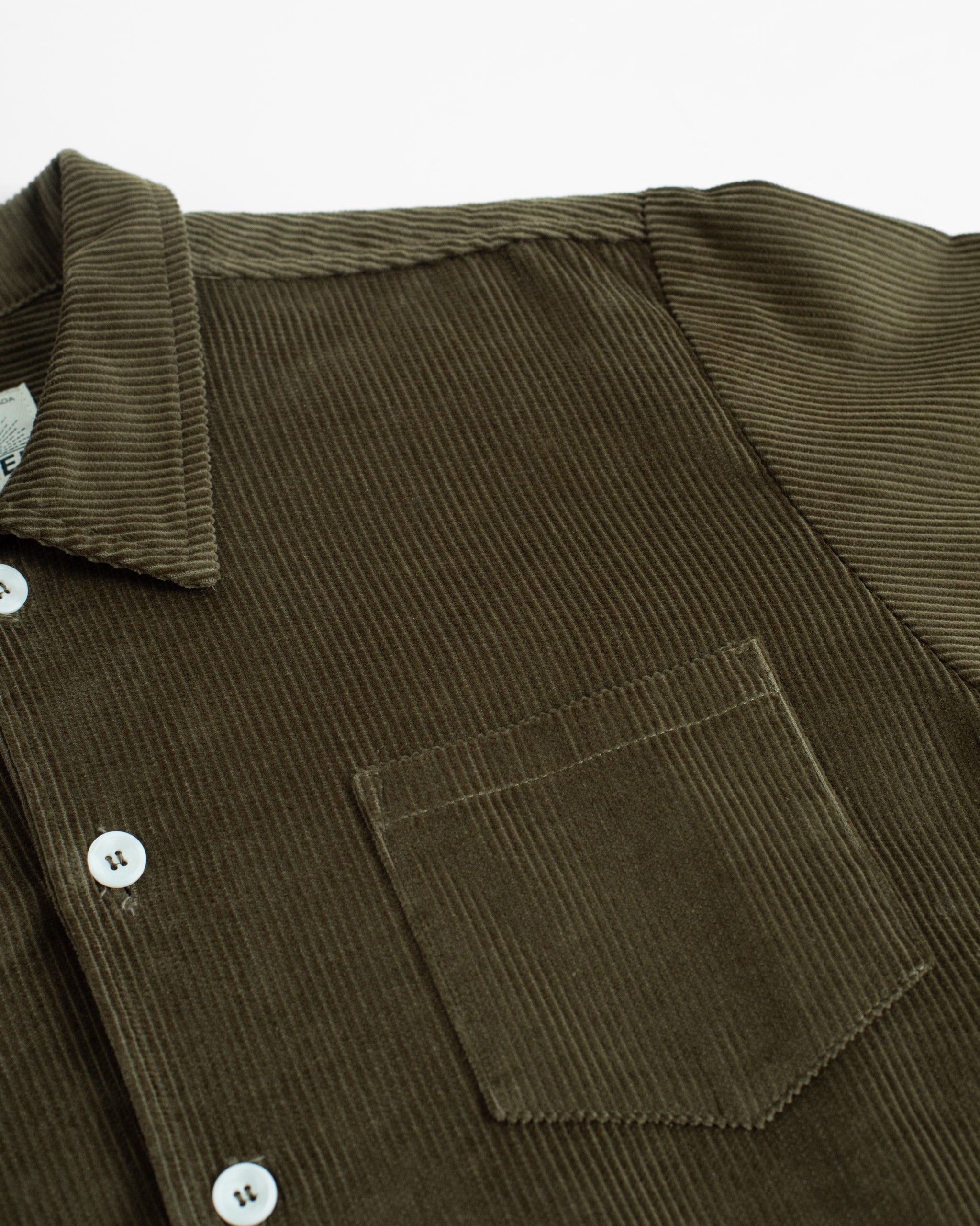 Bather Men's dark olive green corduroy shirt close-up, showing the ribbed 8-wale fabric texture, chest pocket, and white buttons.
