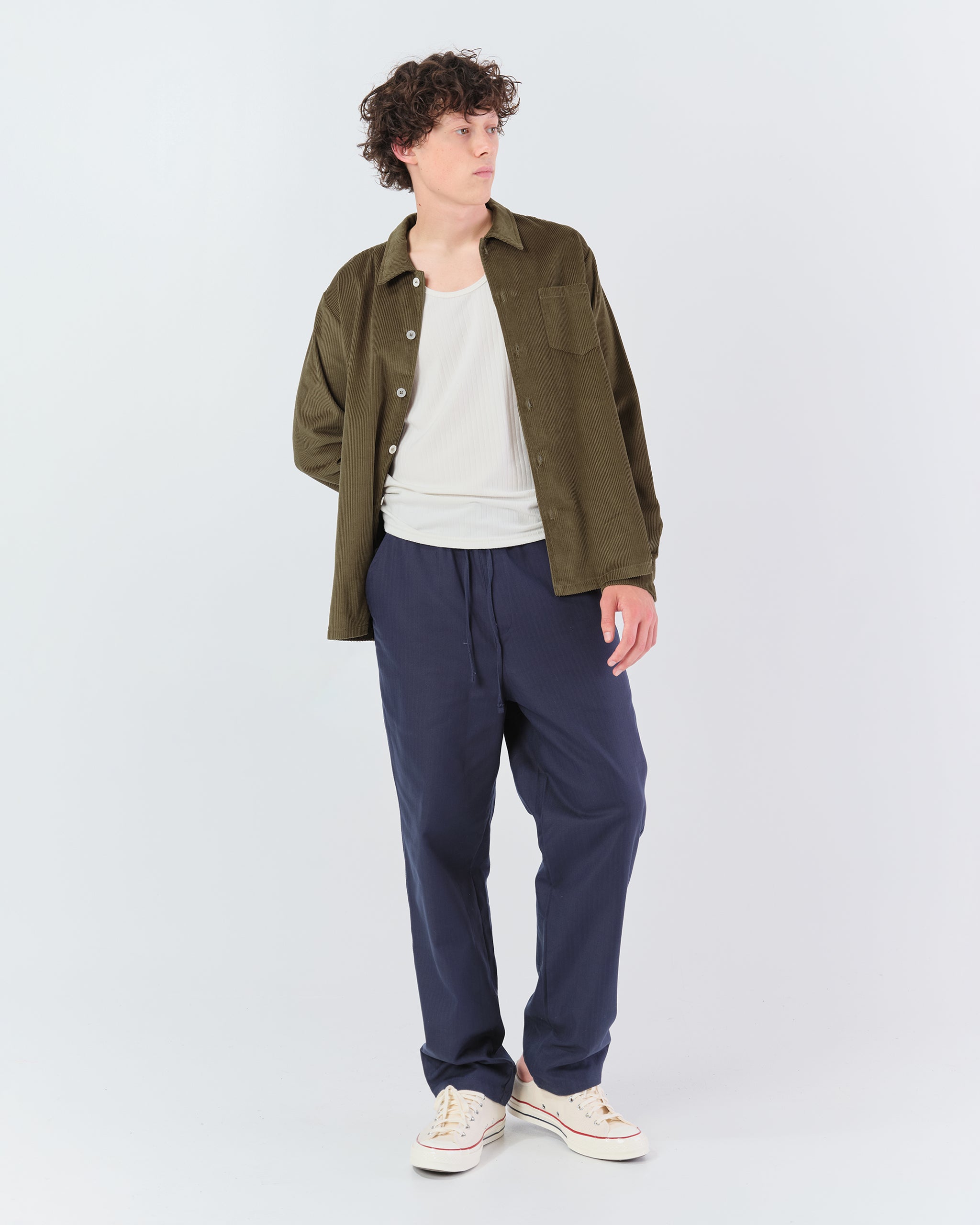 Full-length view of a model wearing the Bather Men's dark olive green corduroy shirt and navy pants.