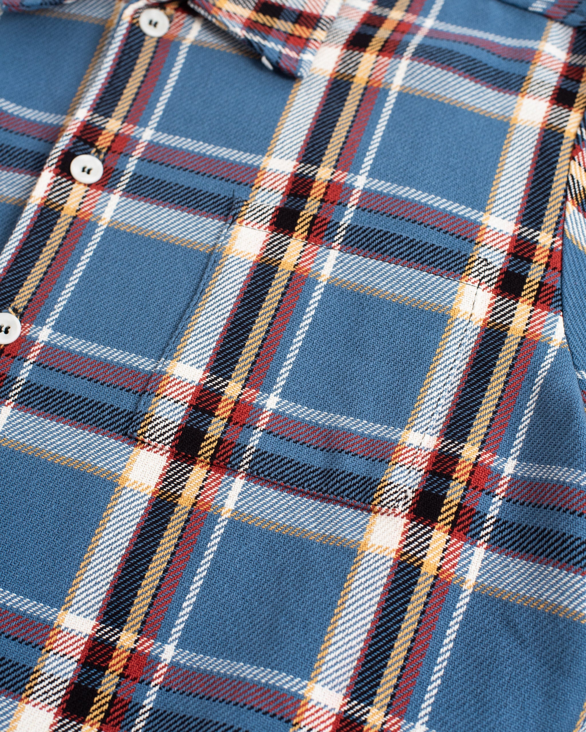 Close-up of the Bather Men's Marlin Plaid Flannel Shirt highlighting the blue and tan checkered fabric texture, white buttons, and durable double-stitched seams.