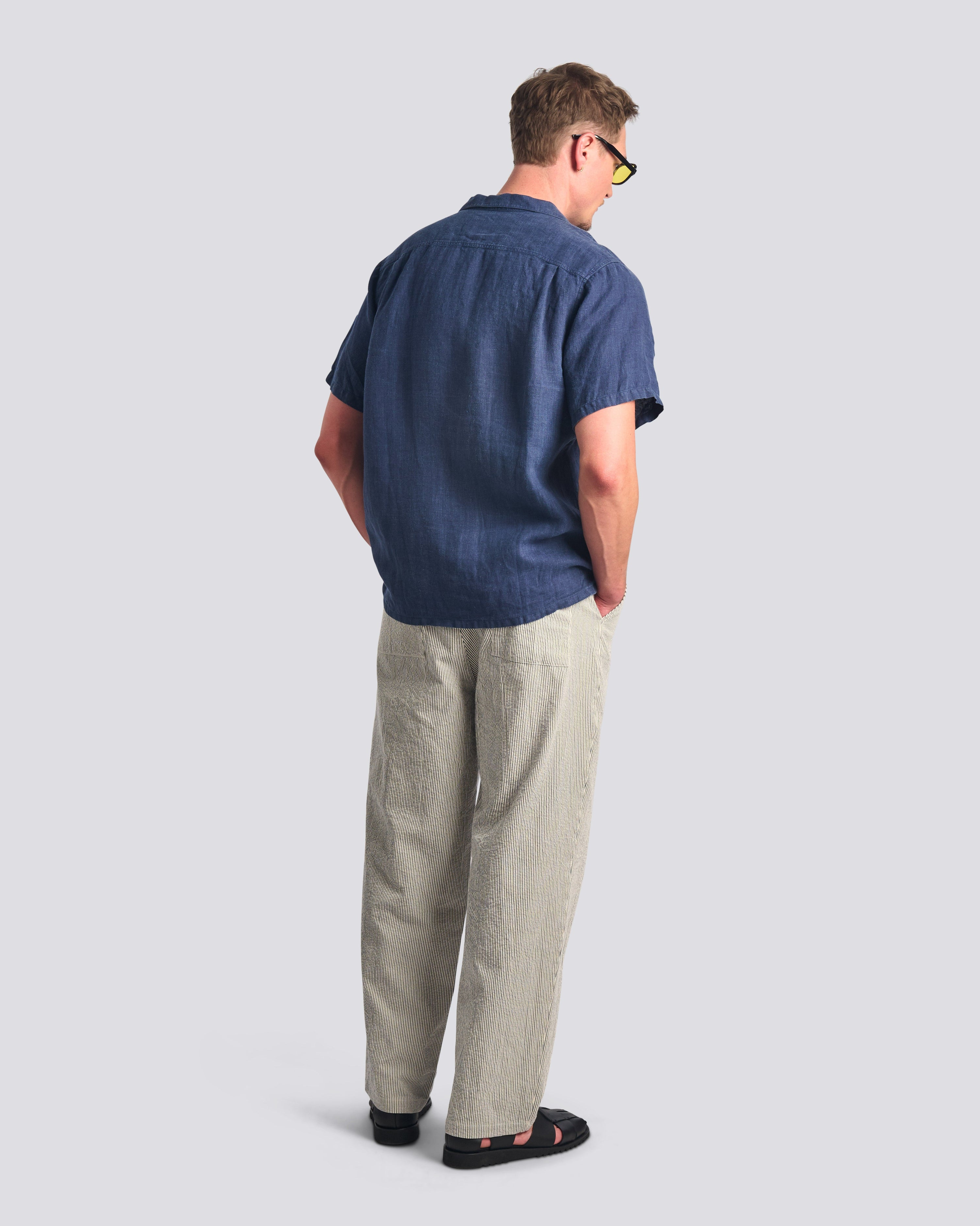 Man wearing a blue shirt and beige pants on a light gray background