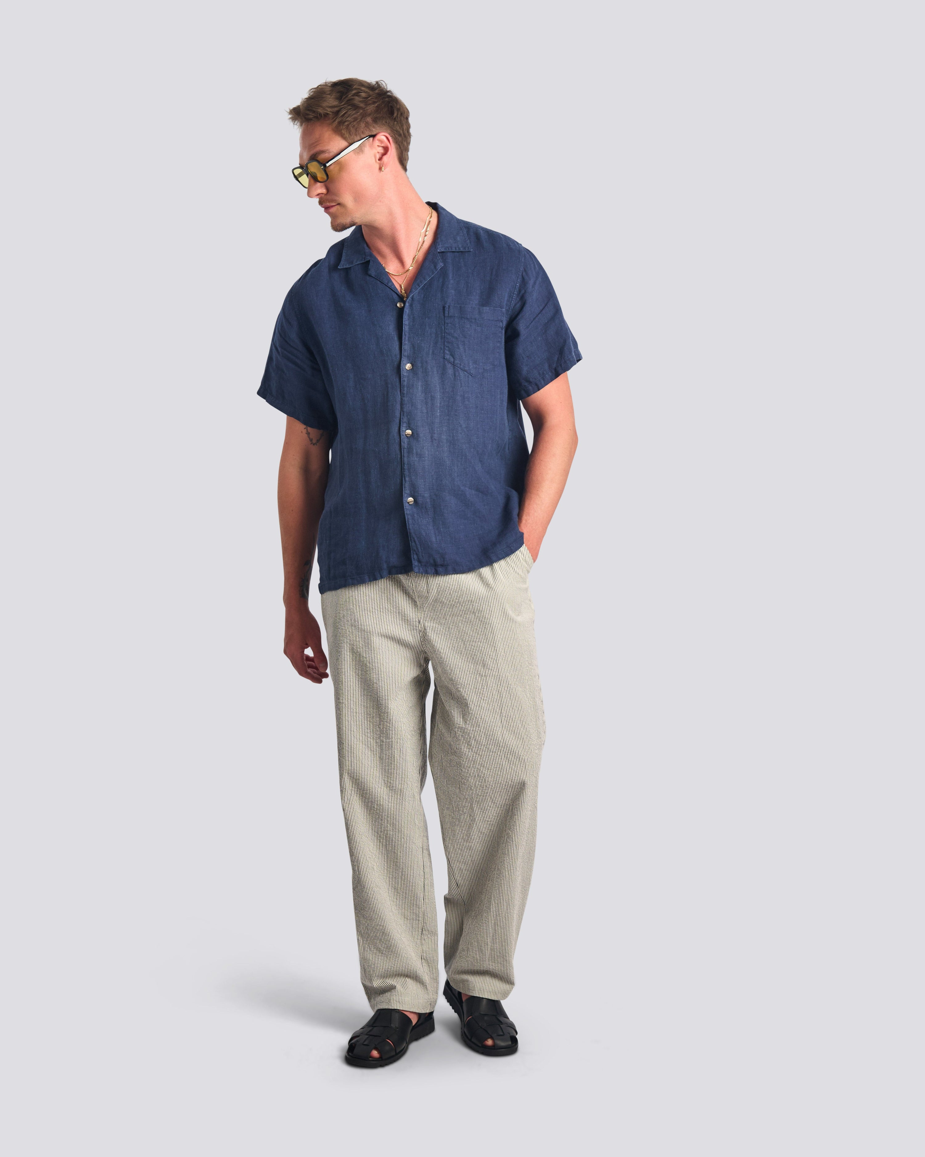 Man wearing a navy button-up shirt and beige pants on a light gray background