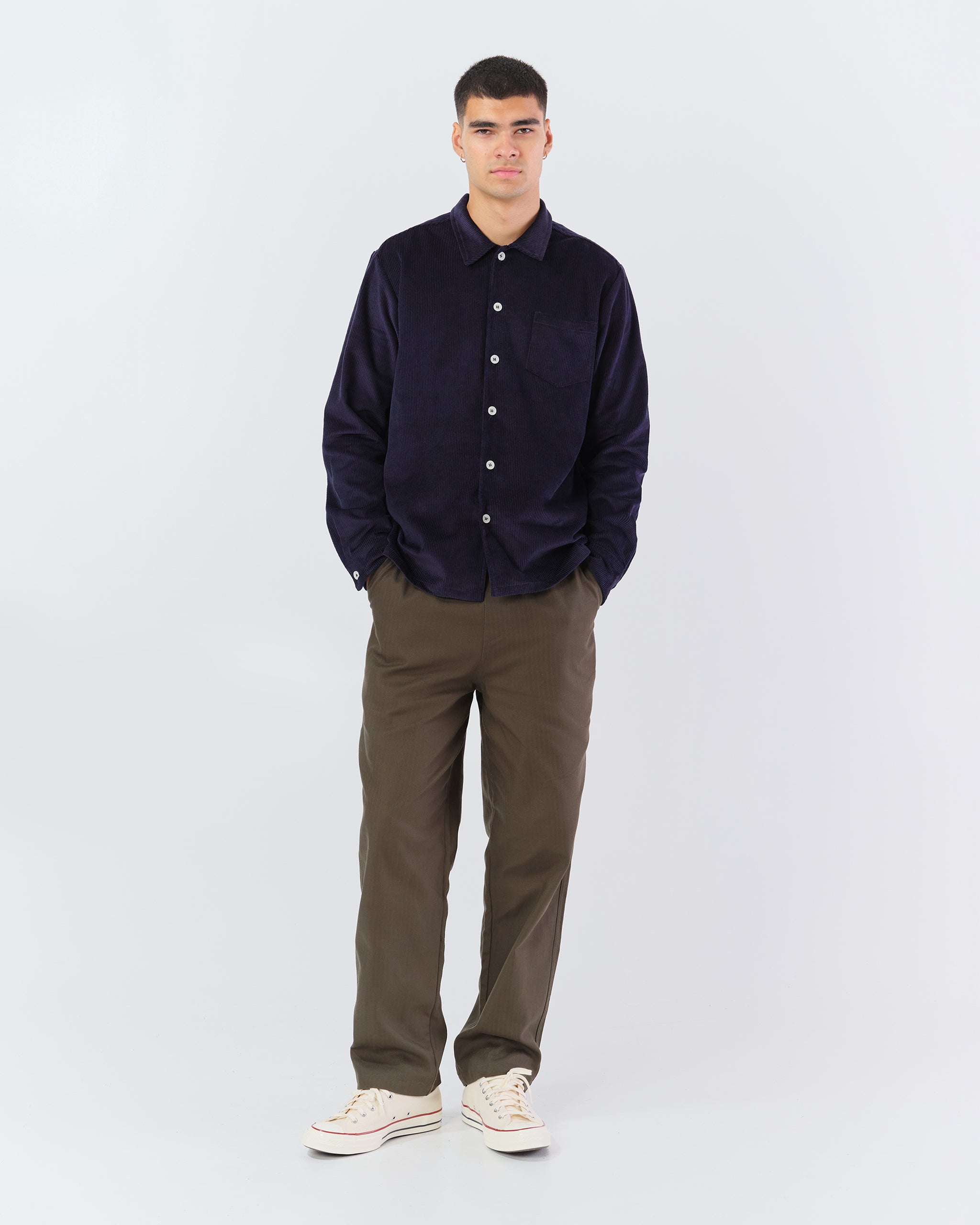 Bather Men's Oxford Corduroy Leisure Shirt in navy blue, buttoned up and styled with olive green trousers and cream sneakers on a model.