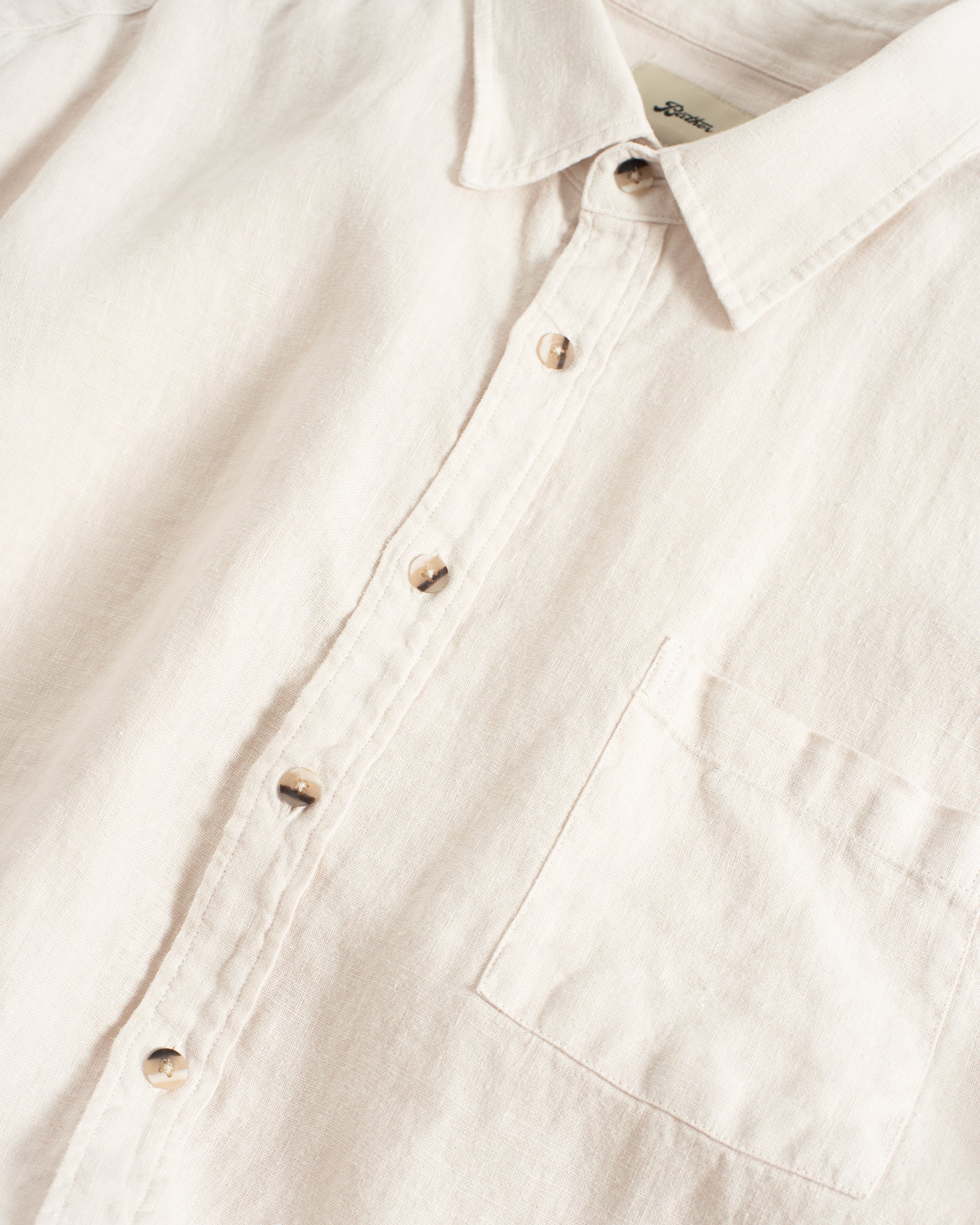 Close-up of the Bather Men's Pearl Linen Leisure Shirt in off-white, showing the textured linen weave, tortoise-shell buttons, and a front chest pocket.