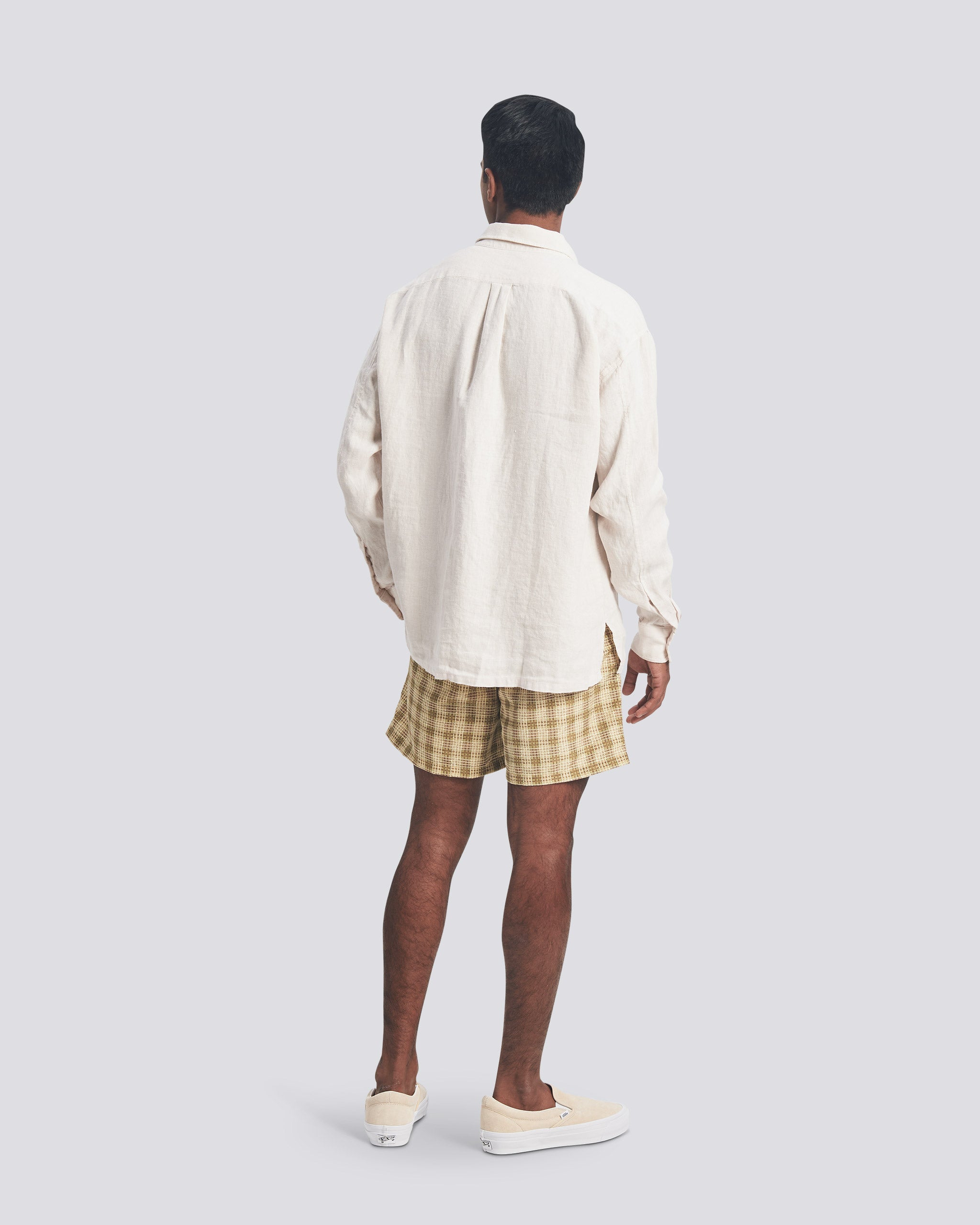 Bather Men's Pearl Linen Leisure Shirt in off-white, showing a rear view of the relaxed fit and natural linen texture on a model wearing checkered swim trunks.