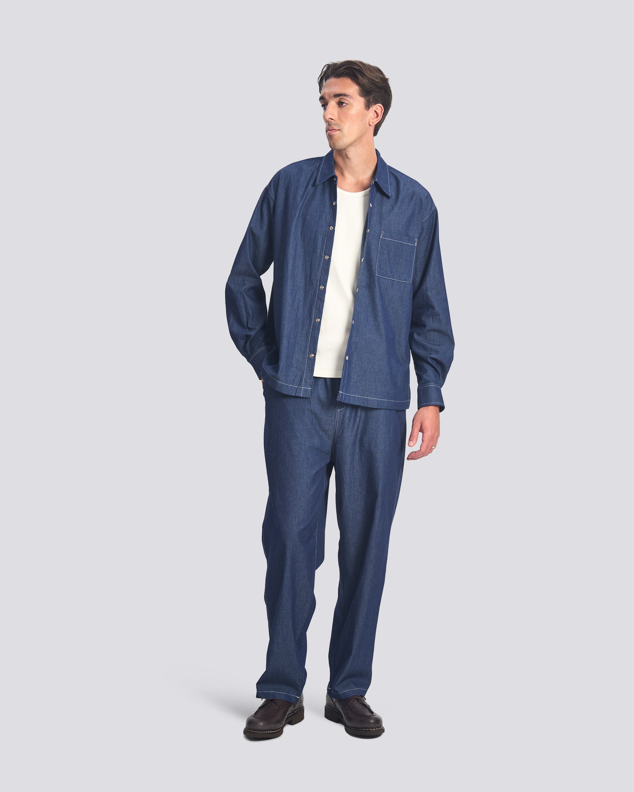 Bather Men's Rinsed Denim Leisure Shirt in dark indigo, styled as a set with matching denim leisure pants over a white t-shirt and black leather shoes on a model.