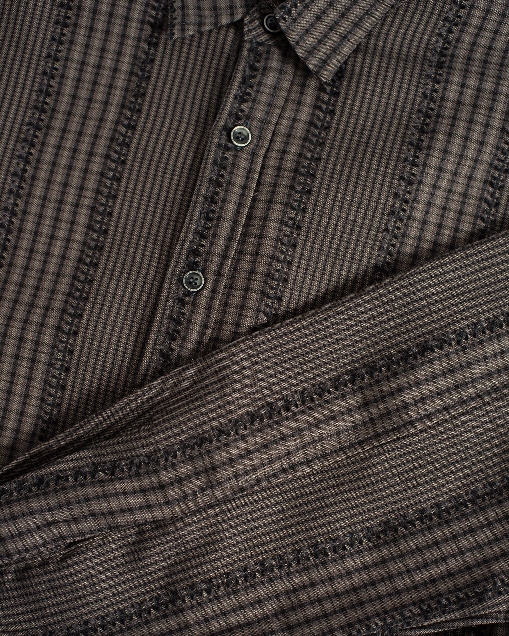 Close-up of the Bather Men's Smoke Fringe Leisure Shirt, highlighting the intricate texture of the charcoal grey Japanese patchwork fabric and the unique fringe detailing along the seams.