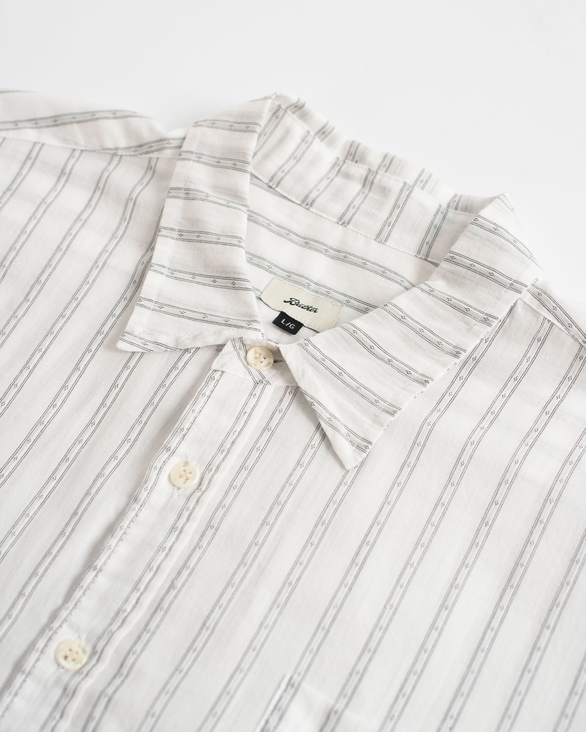 Close-up of the Bather Men's White Dobby Leisure Shirt, highlighting the textured dobby weave with a light blue pinstripe pattern, the open collar, and white buttons.
