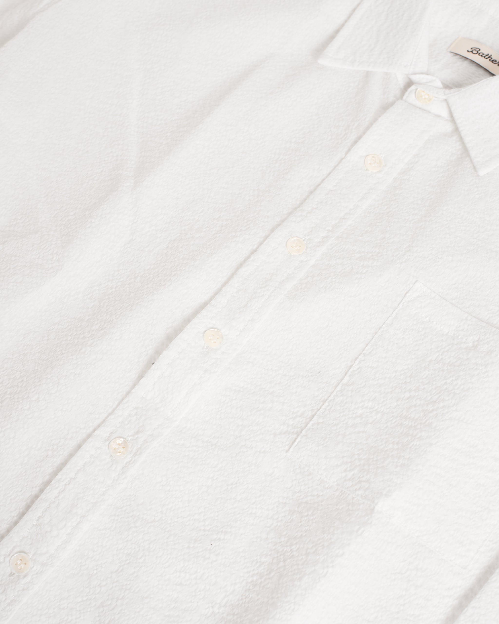 Close-up of the Bather Men's White Ripple Leisure Shirt, highlighting the wavy seersucker texture of the 100% cotton Japanese fabric, an open collar, and a front chest pocket.