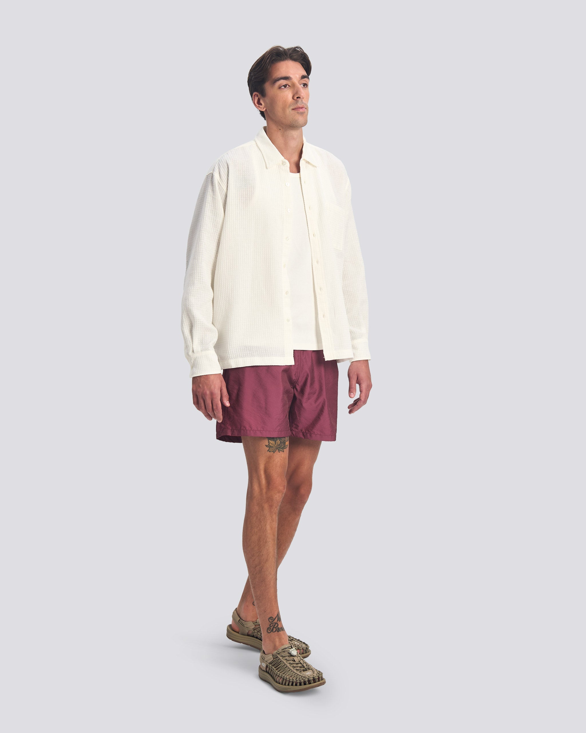 Bather Men’s White Waffle Leisure Shirt styled open over a white tank top with plum-colored swim trunks and olive green patterned loafers on a model.