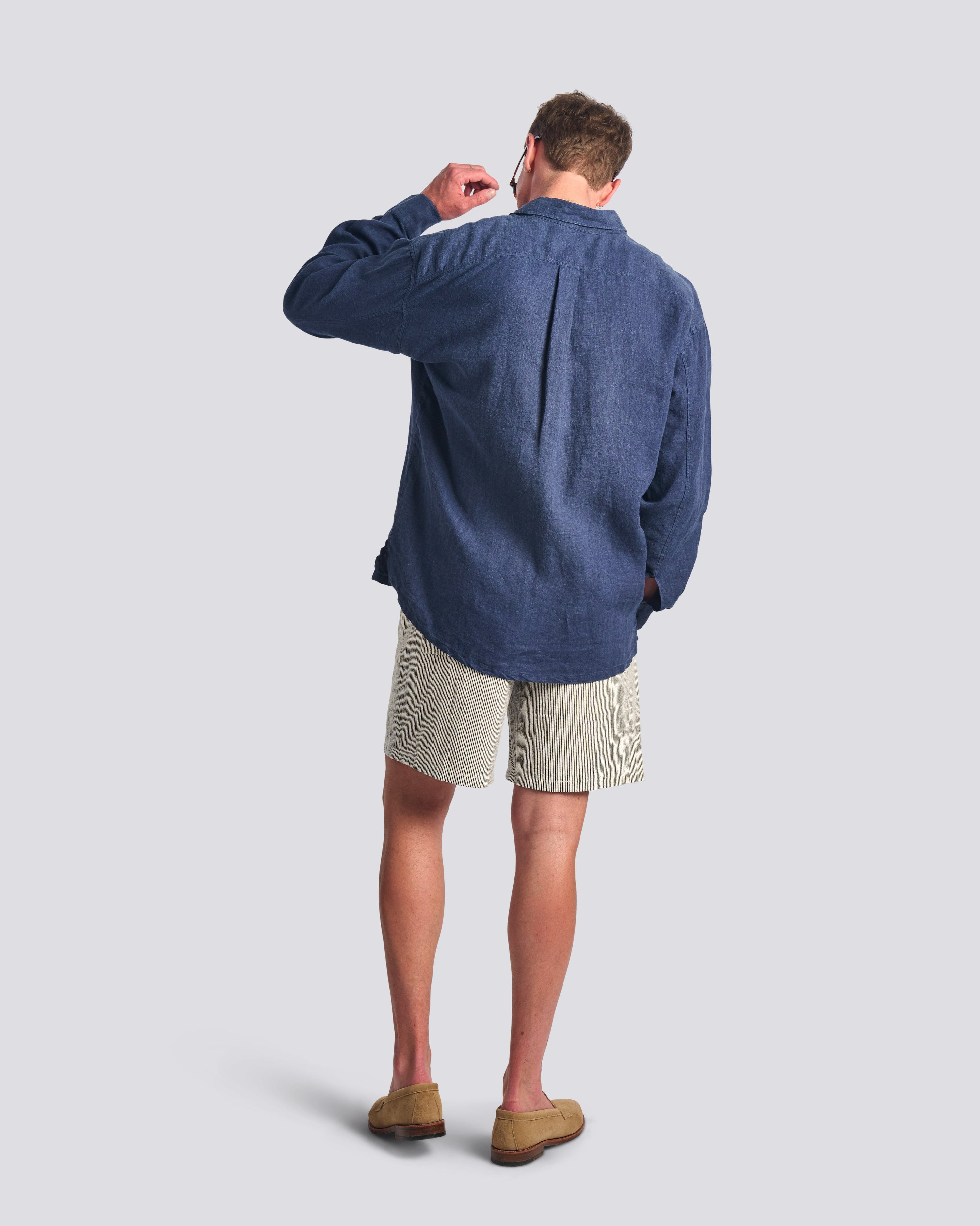 Back view of model wearing Bather men's navy linen  long sleeve shirt and navy pinstripe short