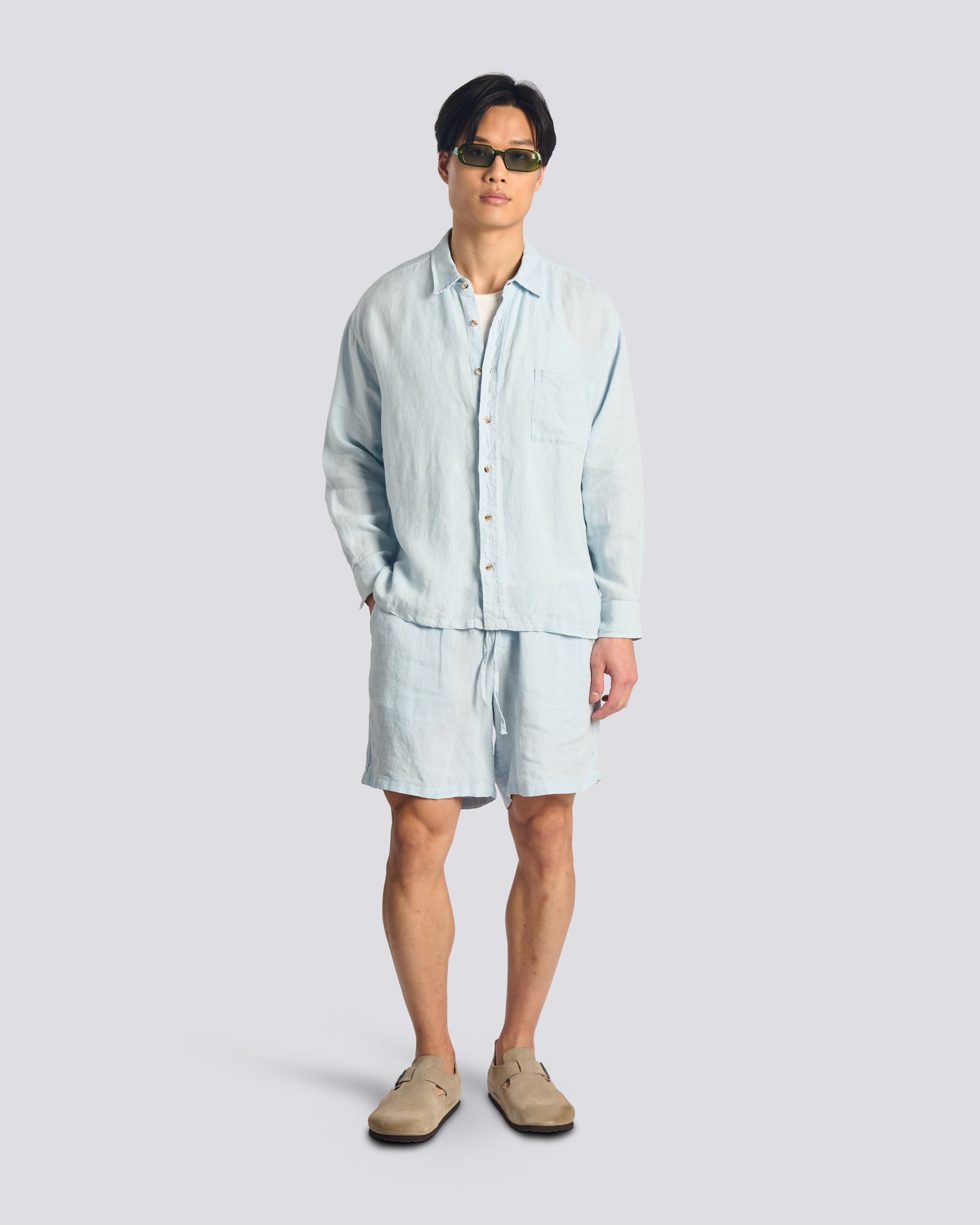 Model wearing bather men's light blue linen shorts with drawstring and matching button-up shirt