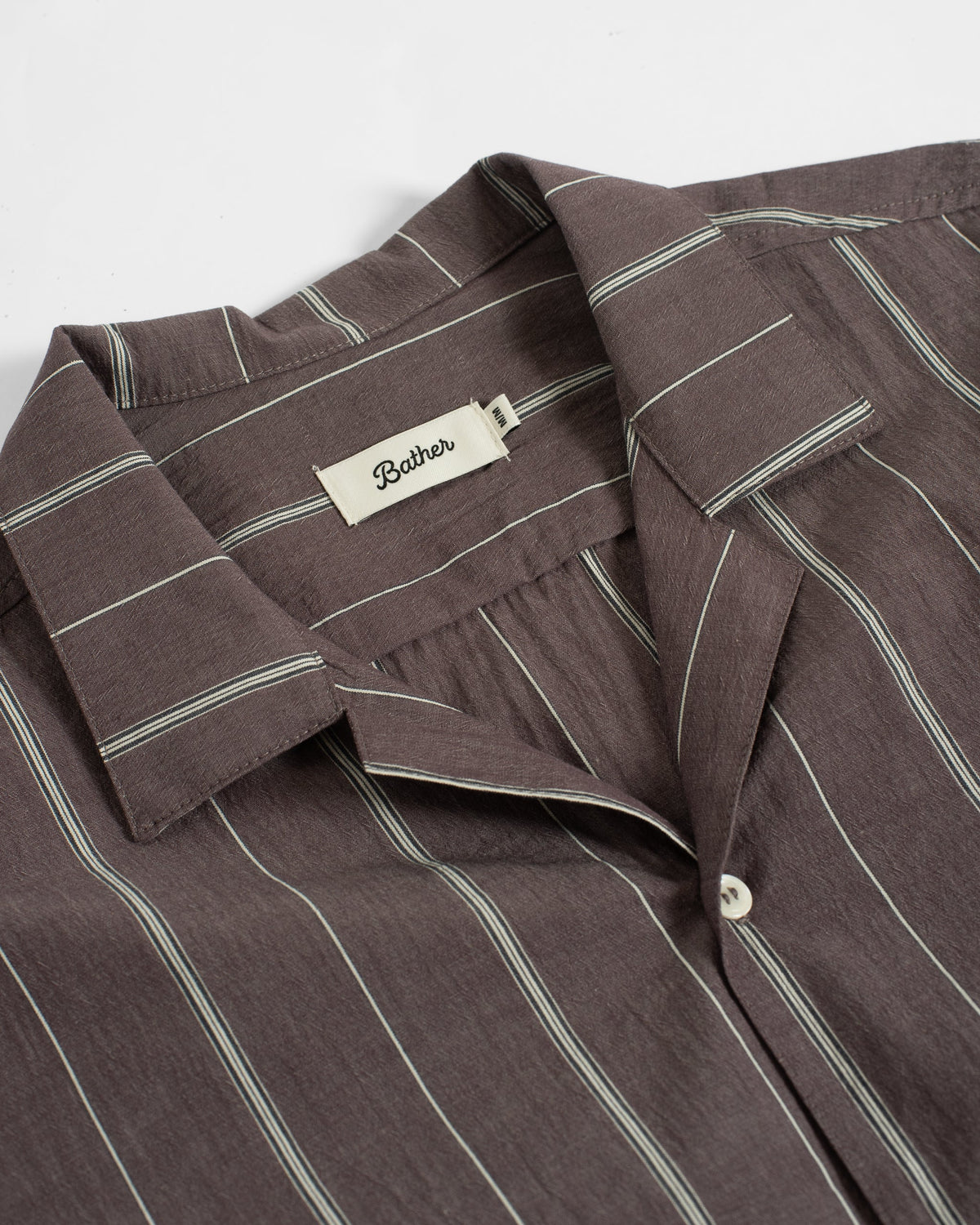 A close-up of a brown pinstriped button-down shirt by Bath & Body, showing the collar, inner neck label, and a white button.