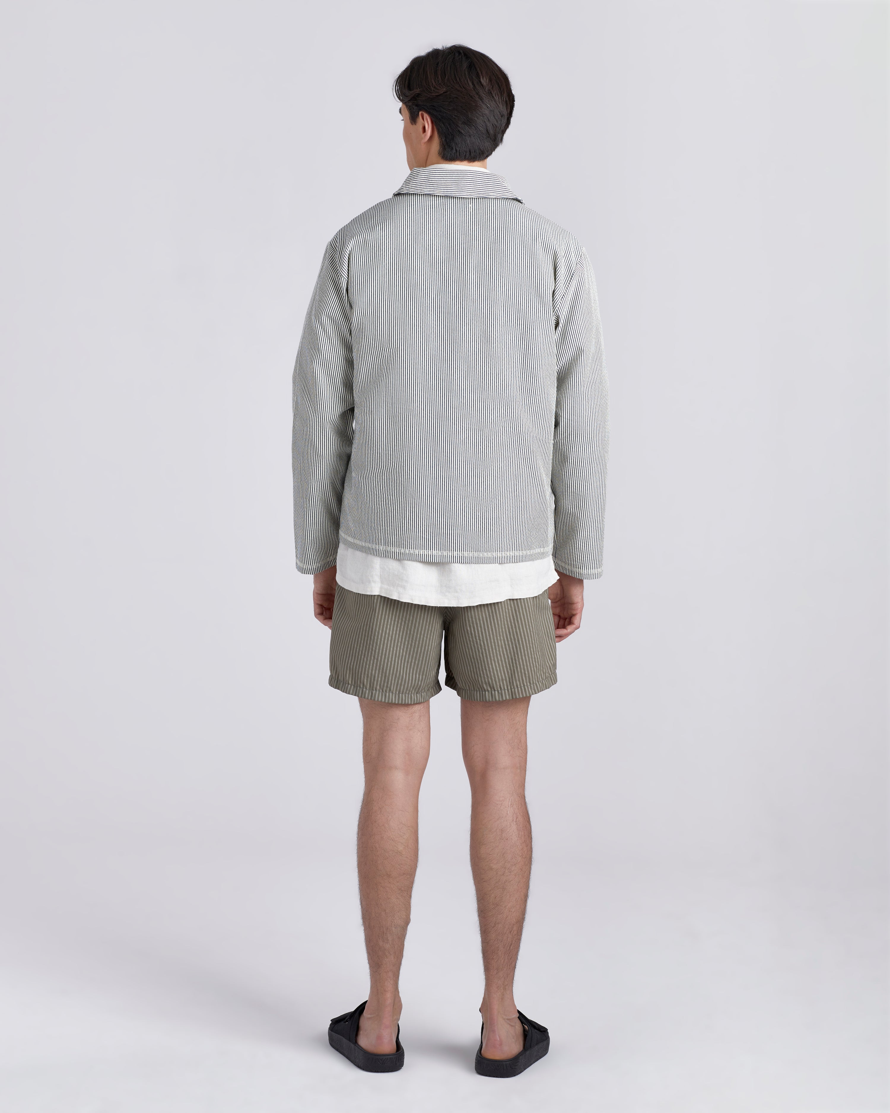 Back of male model wearing a Bather navy pinstripe tour jacket featuring a two-way front zipper with matching navy Bather pin strip pants.