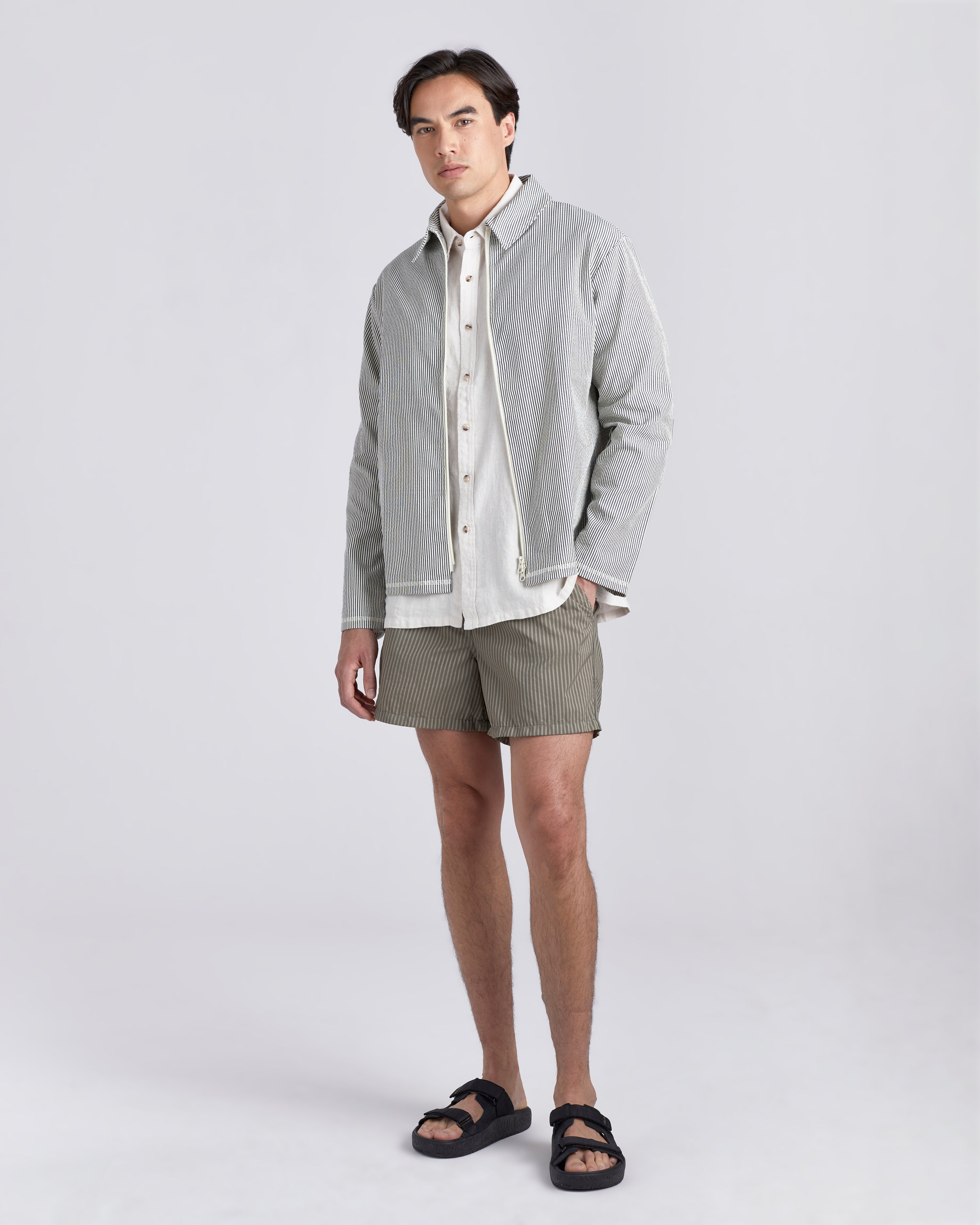 Male model wearing a Bather navy pinstripe tour jacket featuring a two-way front zipper with matching navy Bather pin strip pants.