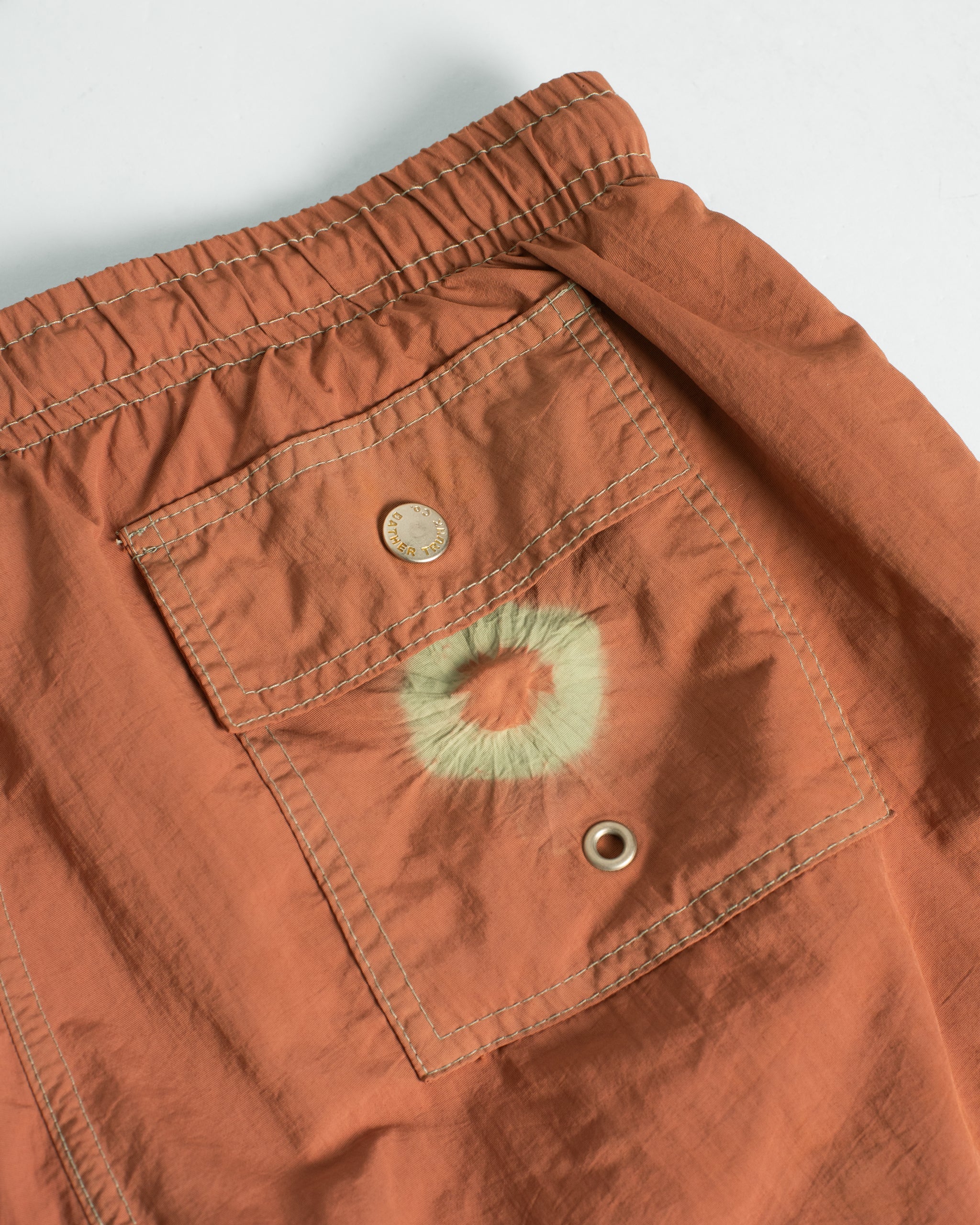 Close-up of an orange swim short with a pocket and button on a light gray background