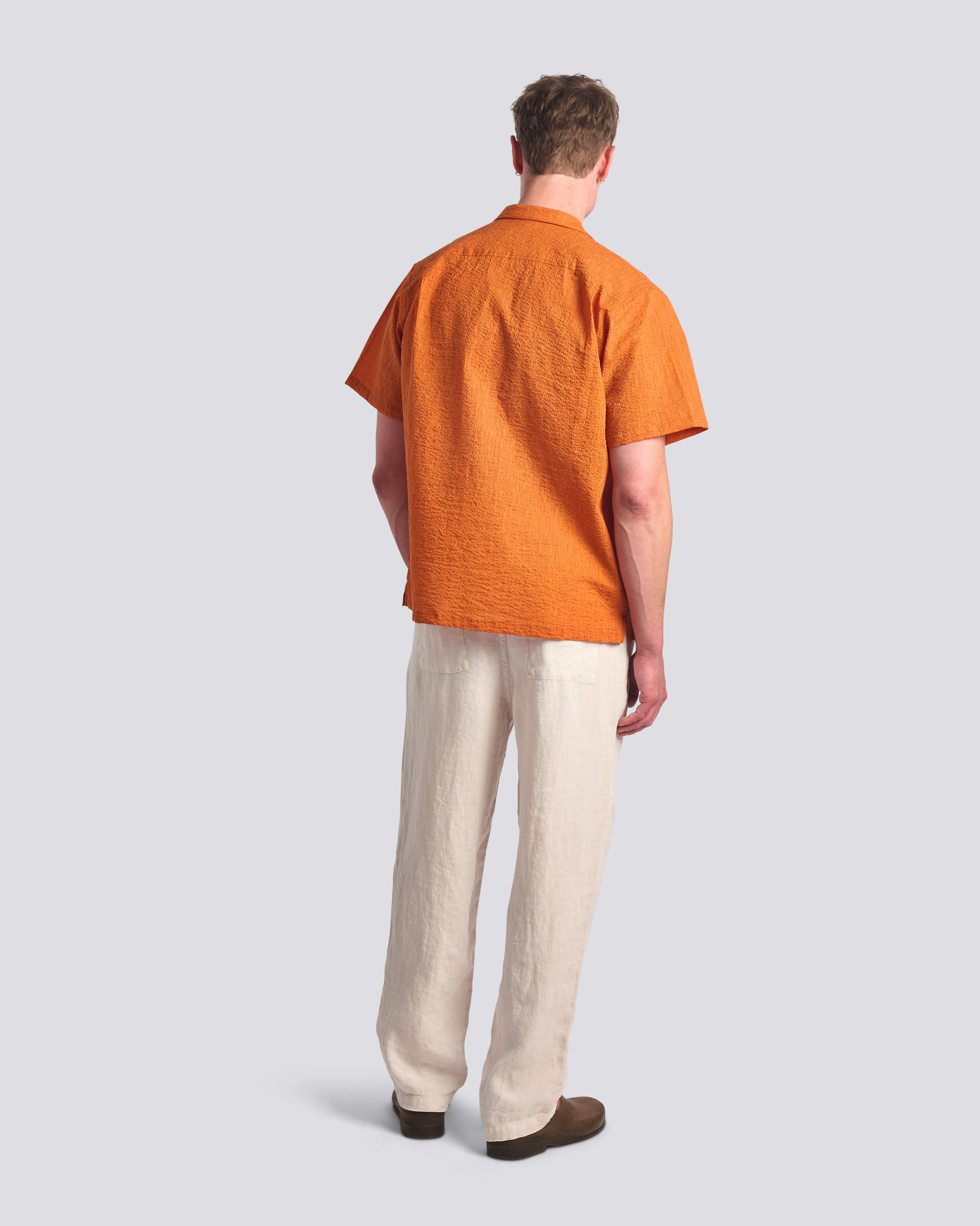 Back of male model wearing a Bather Men's Cantaloupe Ripple Leisure Shirt in a relaxed fit with a straight hem, styled for a summer vacation look.