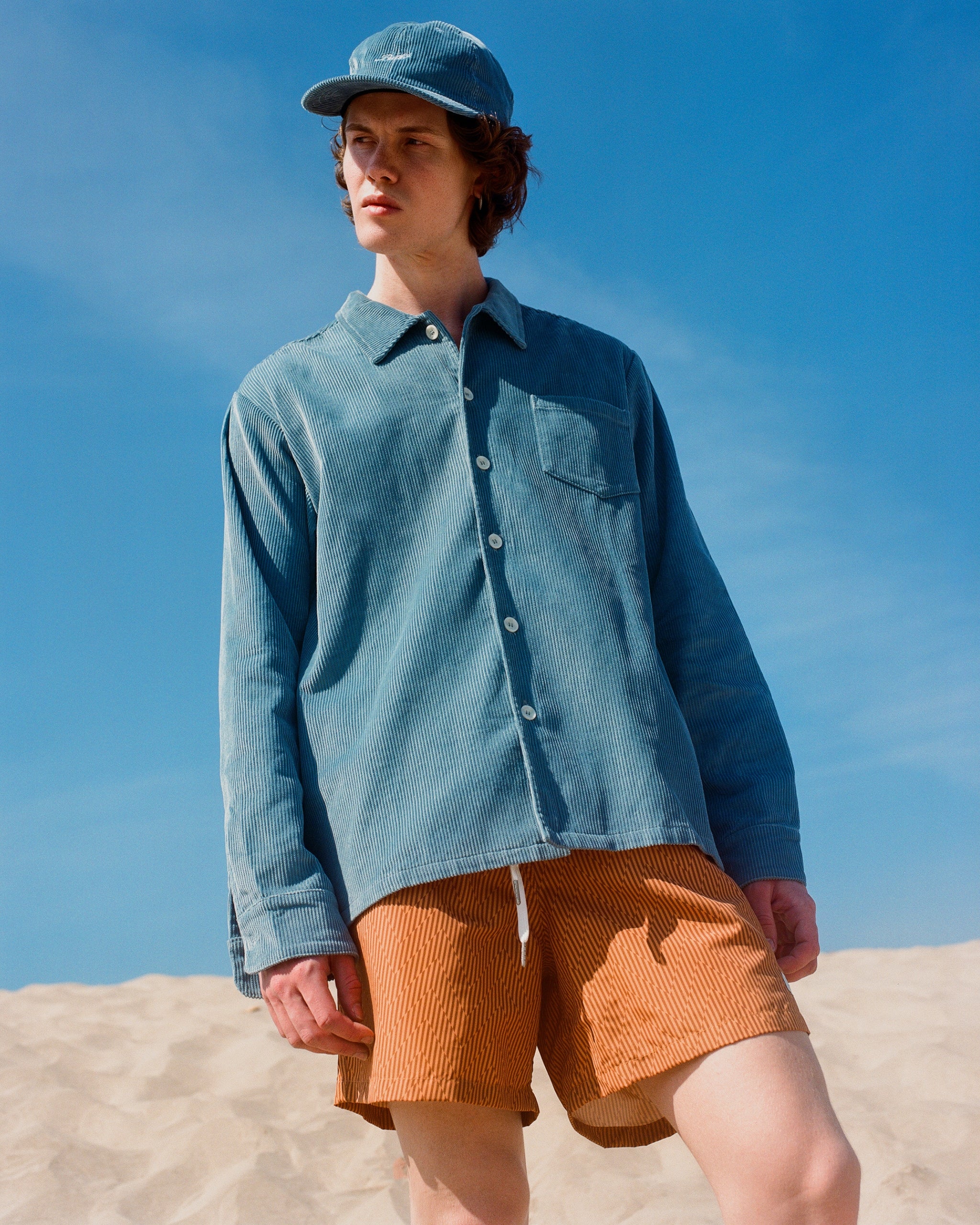 Male model wearing a blue corduroy hat and shirt with orange swim trunks