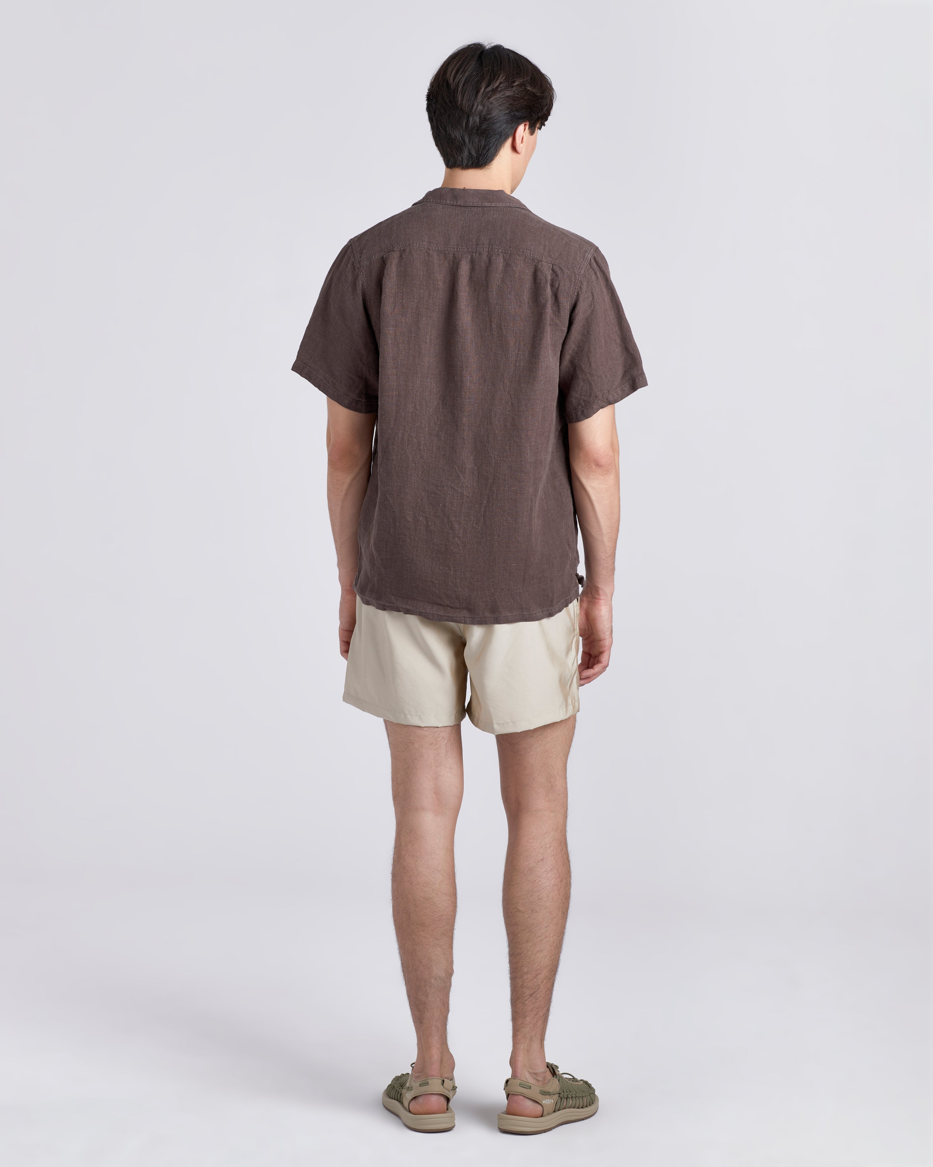 Back of man in brown Bather camp shirt wearing shiny white swim trunk featuring an elastic drawstring waistband on white background