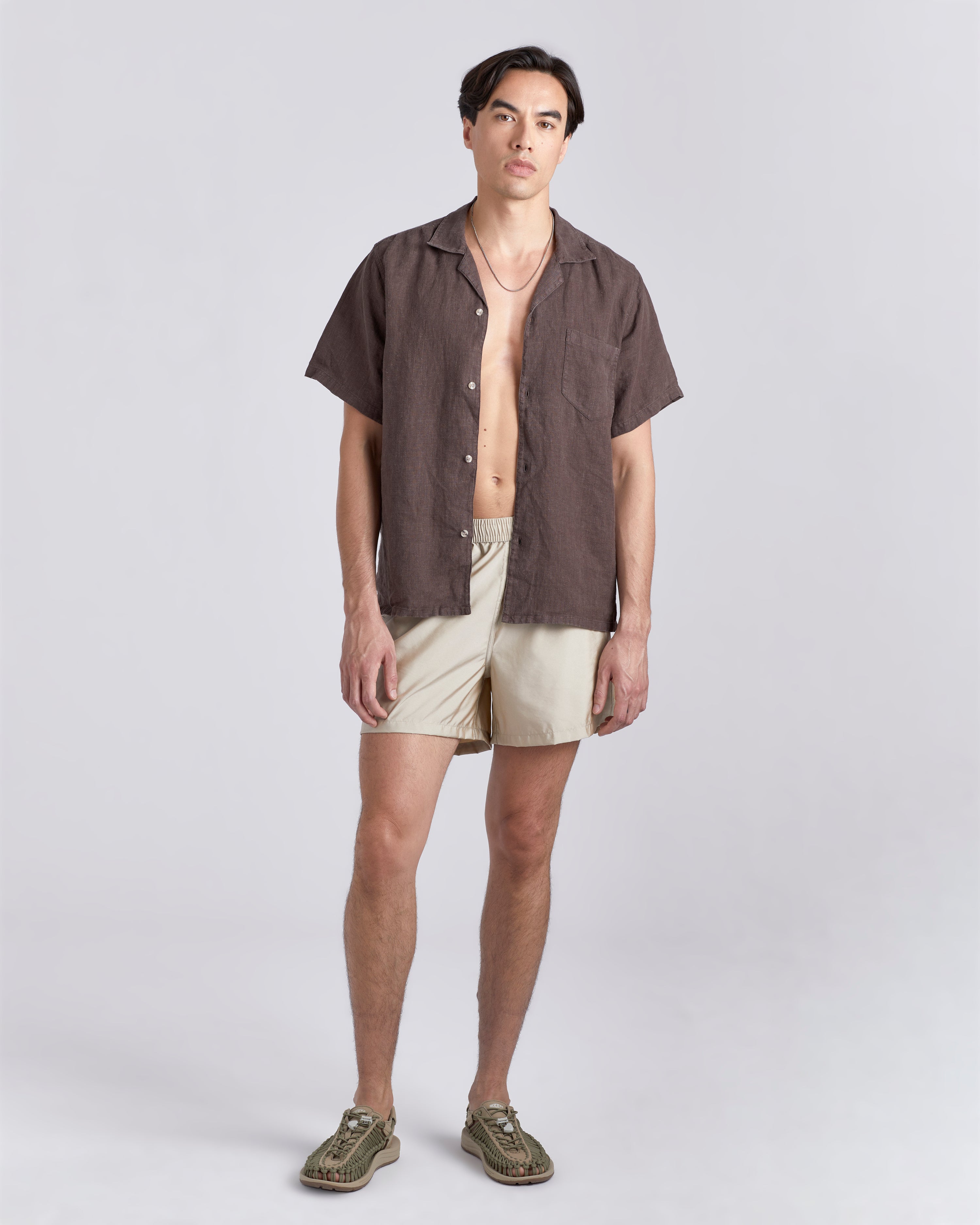 Man in brown Bather camp shirt wearing shiny white swim trunk featuring an elastic drawstring waistband on white background