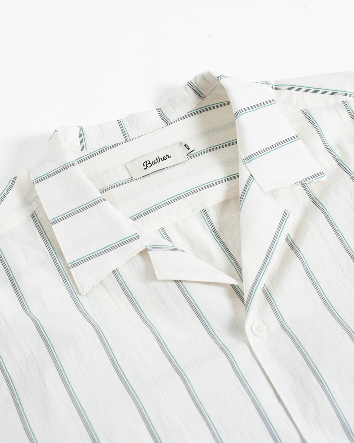 A close-up of a collared button-front shirt in off-white fabric with thin vertical light blue stripes. The inner neck label reads 'Bathes'.
