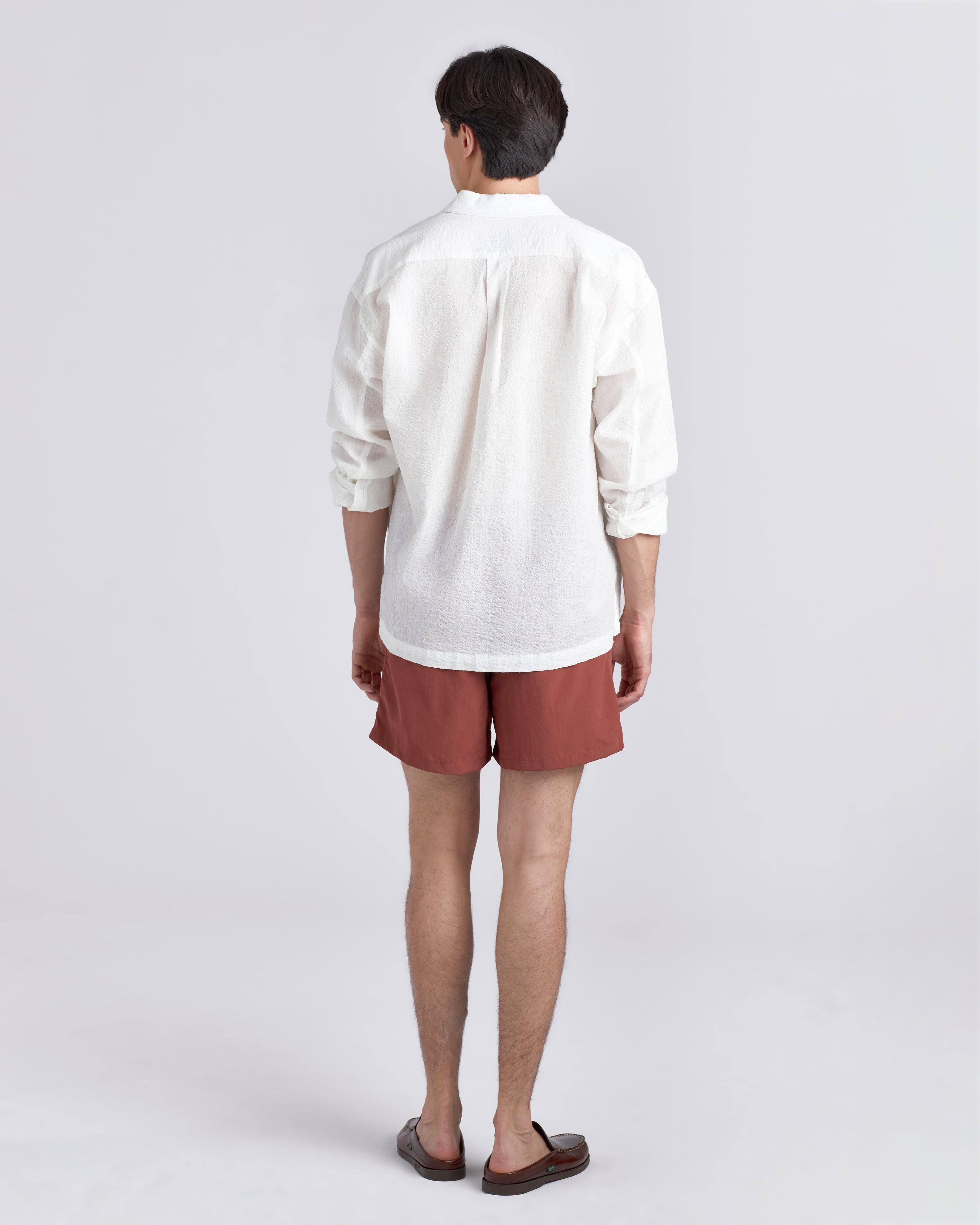 Back of male model in White linen Bather leisure shirt wearing solid red swim trunk featuring an elastic drawstring waistband on white background