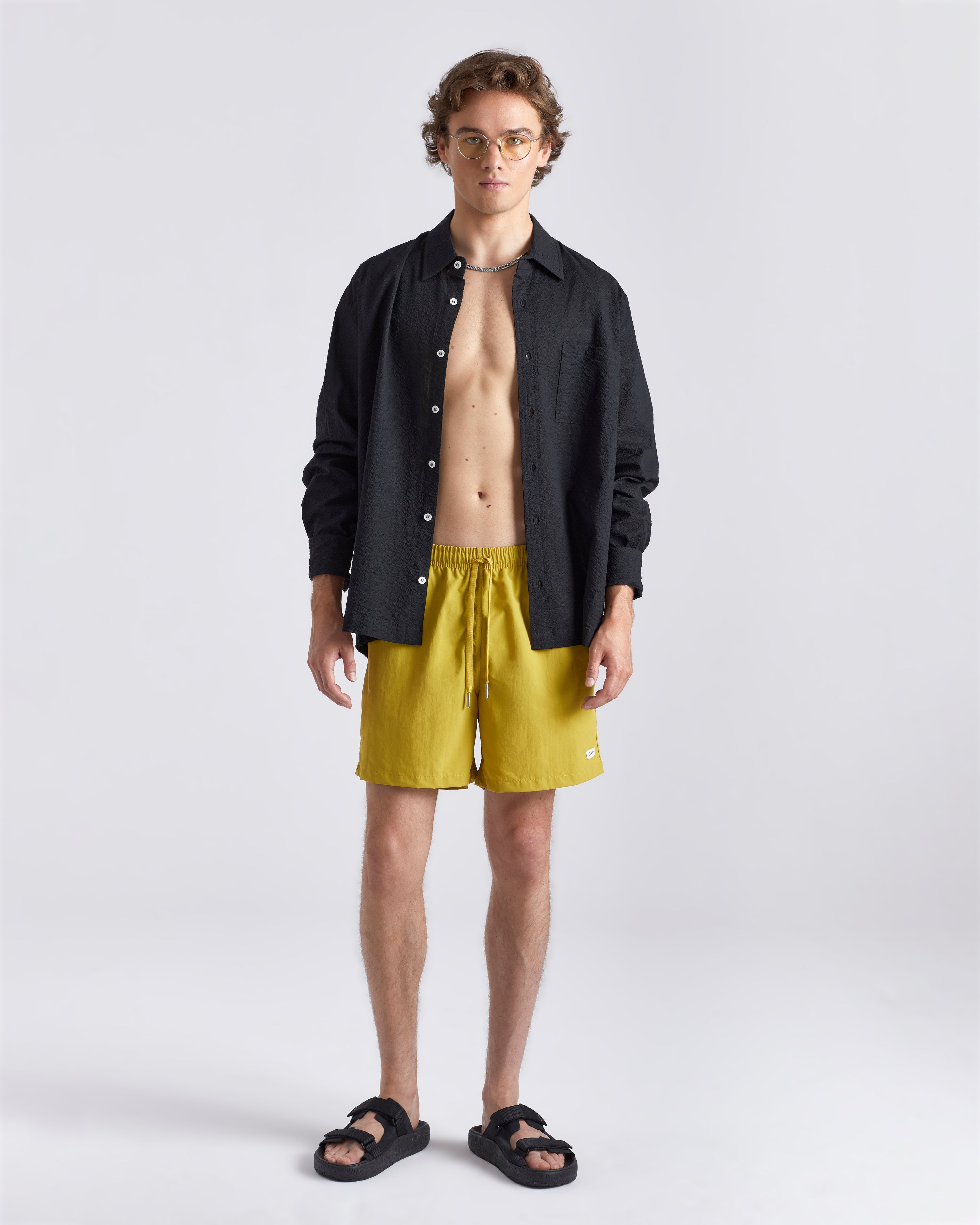 Man in black linen Bather leisure shirt wearing solid yellow swim trunk featuring an elastic drawstring waistband on white background