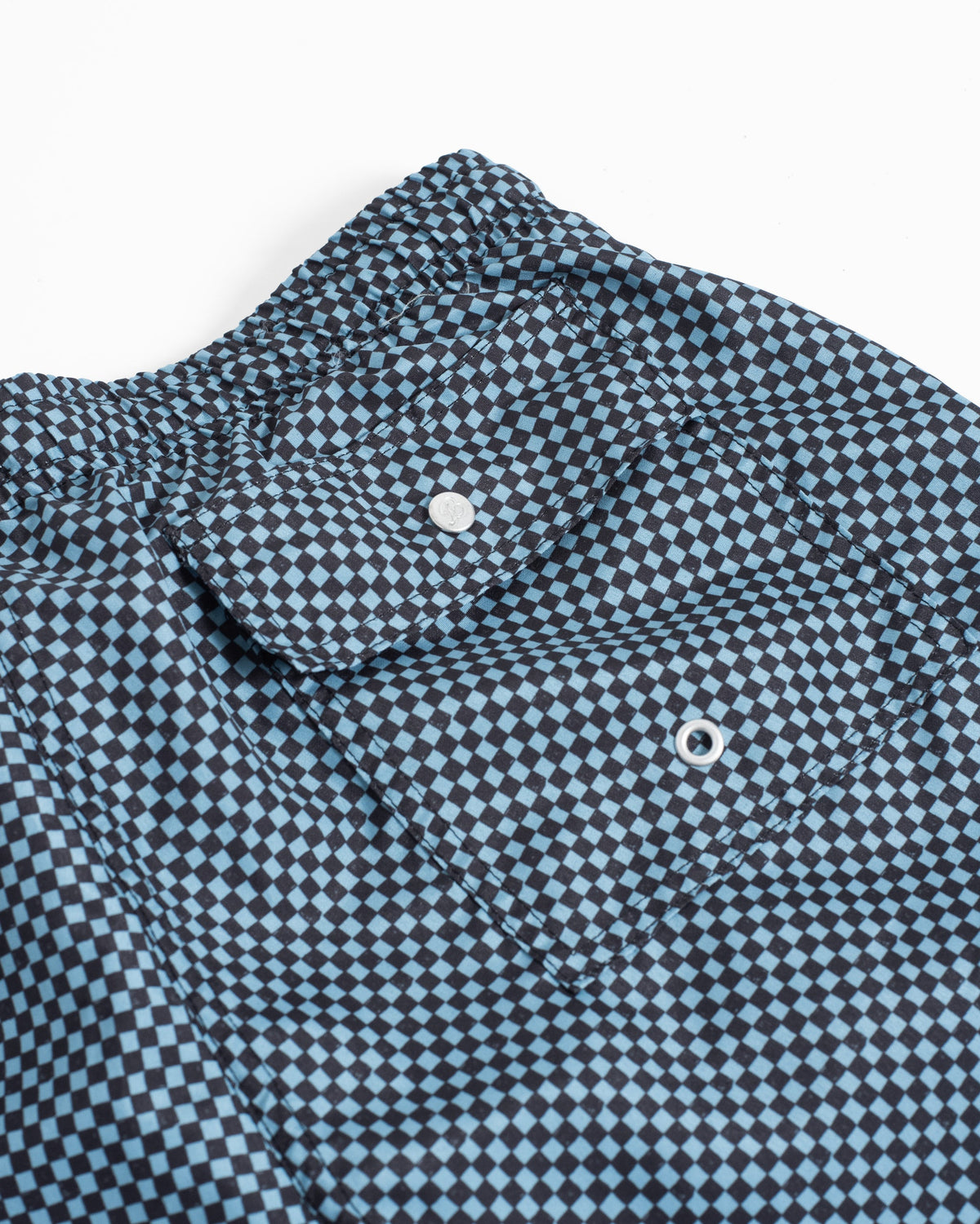 Close-up of a blue and white checkerboard patterned garment, showing part of the collar, button closure, and fabric texture against a plain white background.