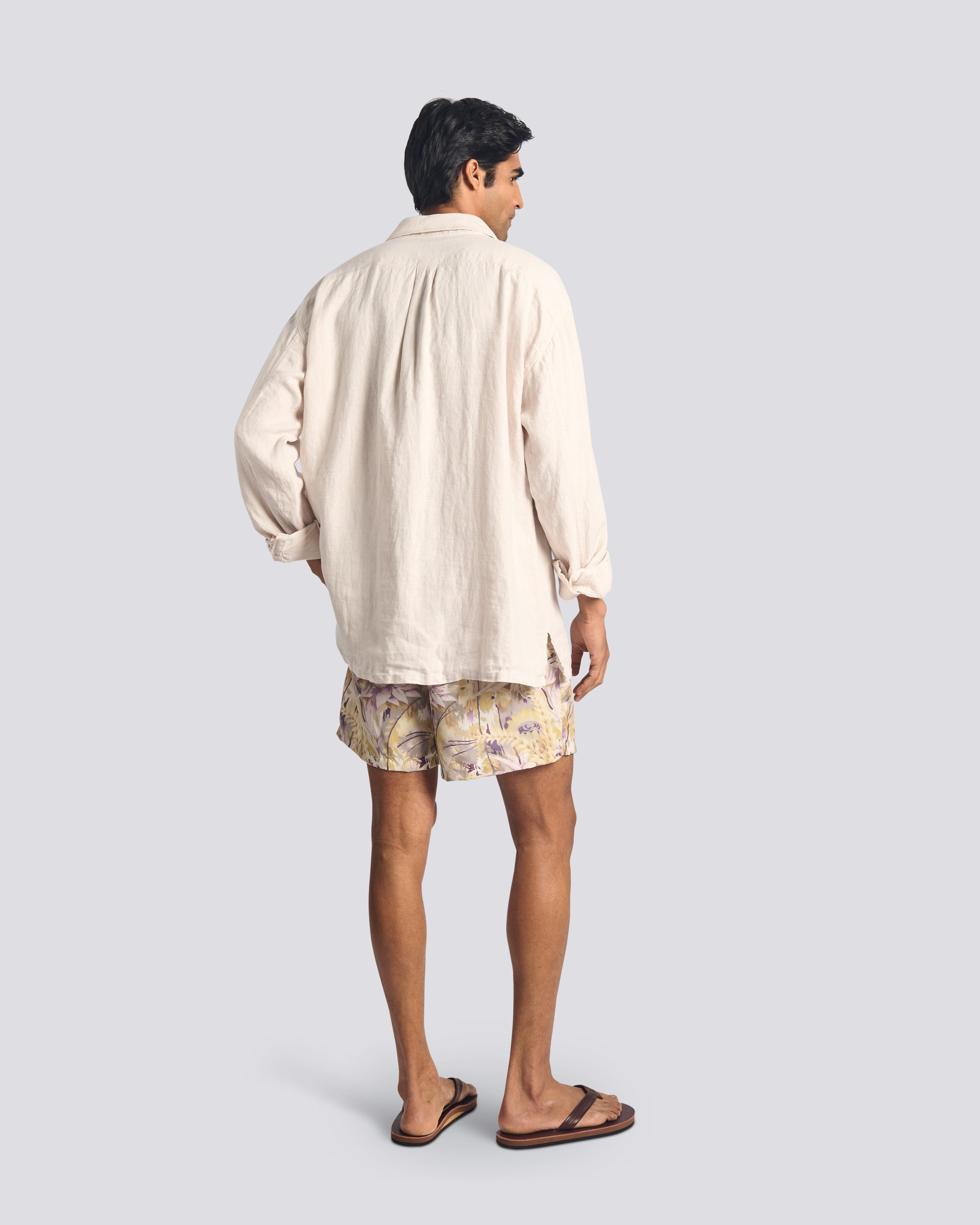 Model wearing men’s tropical floral swim trunks with a Bather cream linen leisure shirt