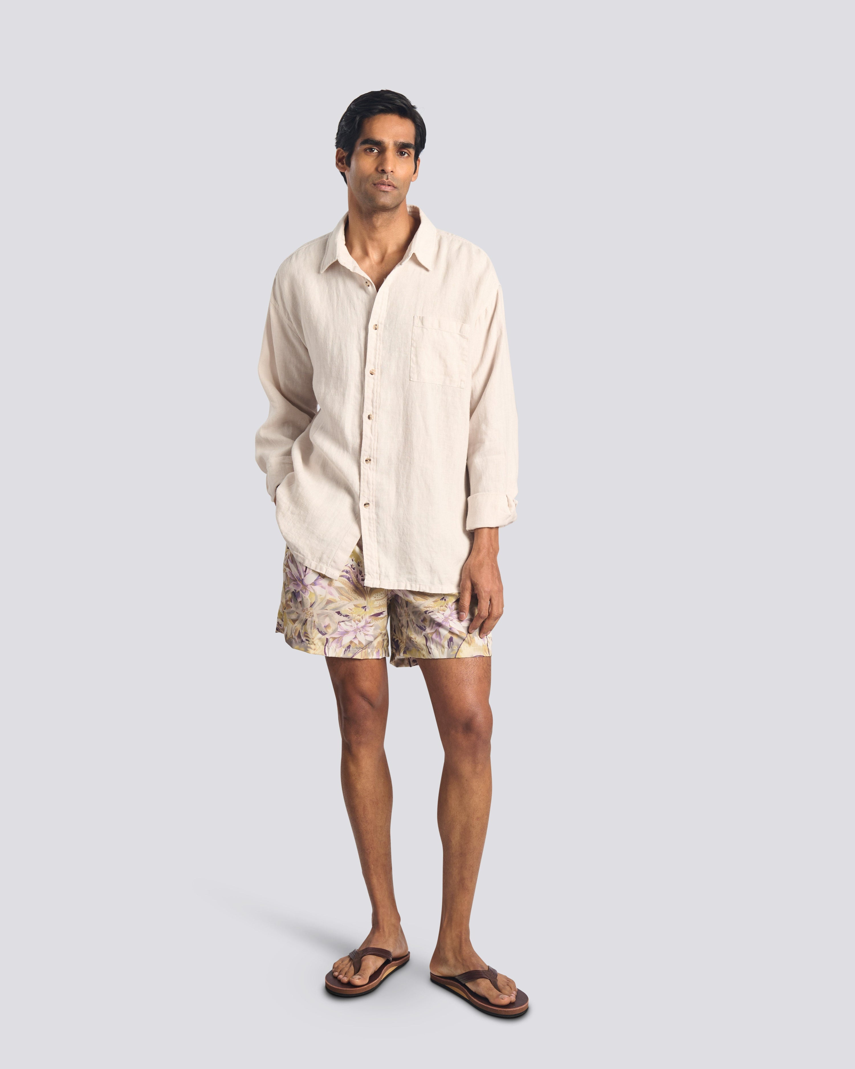 Model wearing men’s tropical floral swim trunks with a Bather cream linen leisure shirt