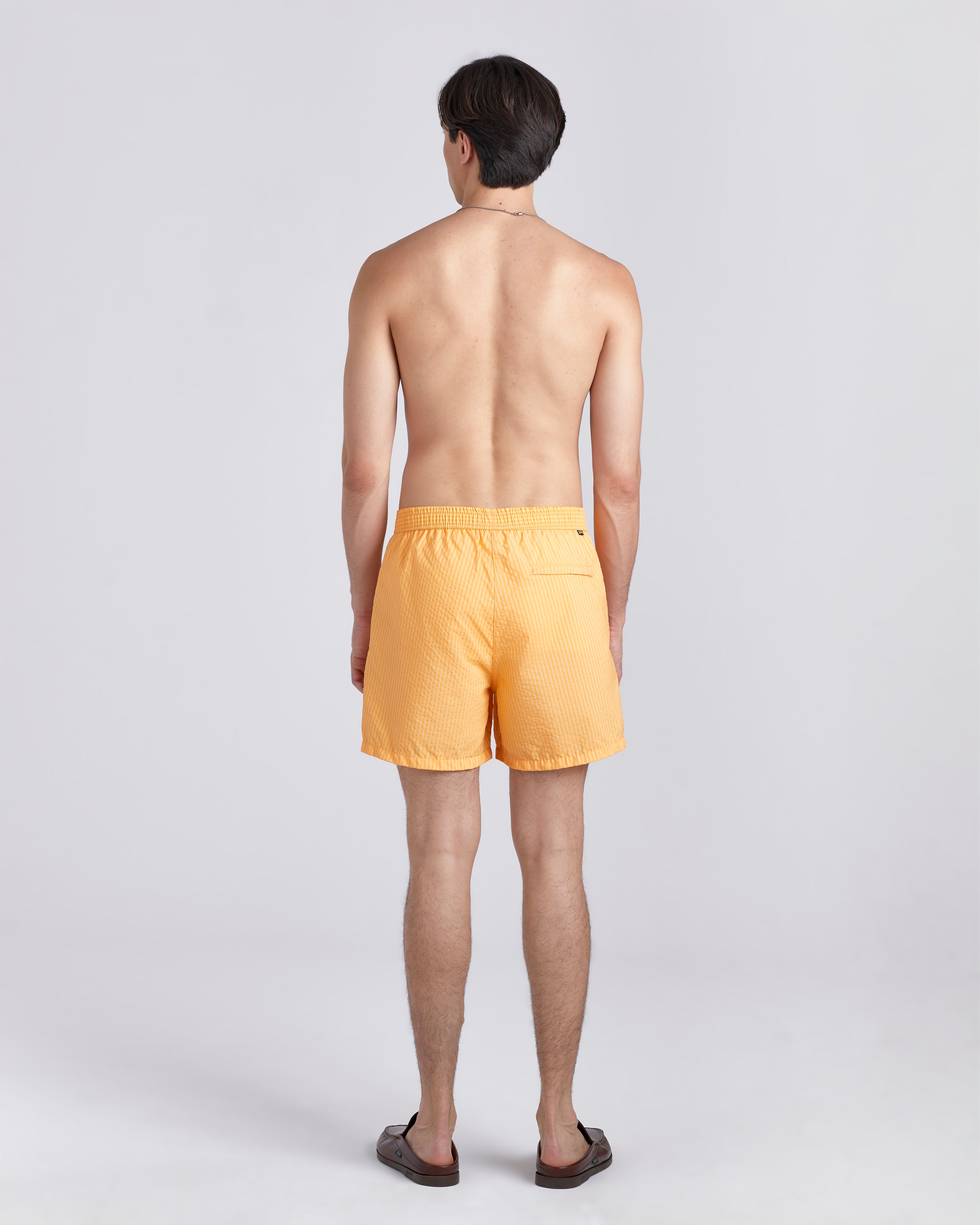Back of shirtless male model wearing yellow swim trunk with a subtle stripe featuring an elastic drawstring waistband on white background