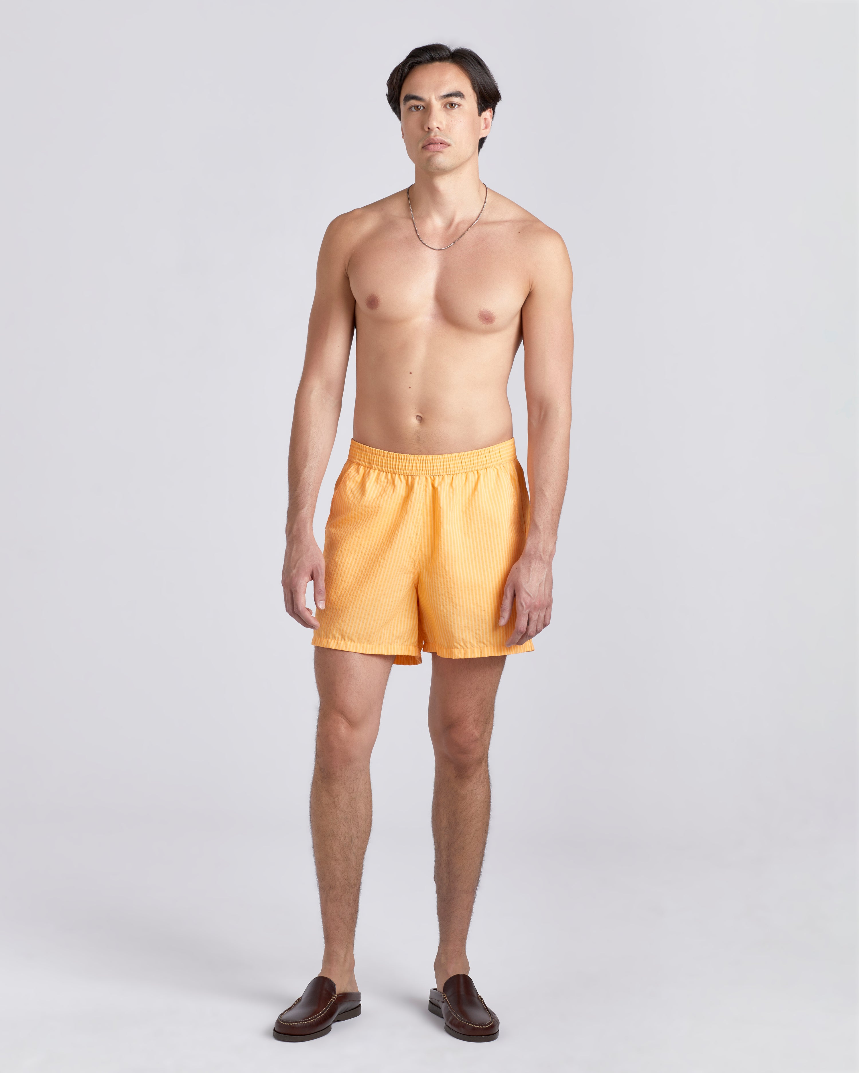 Shirtless male model wearing yellow swim trunk with a subtle stripe featuring an elastic drawstring waistband on white background
