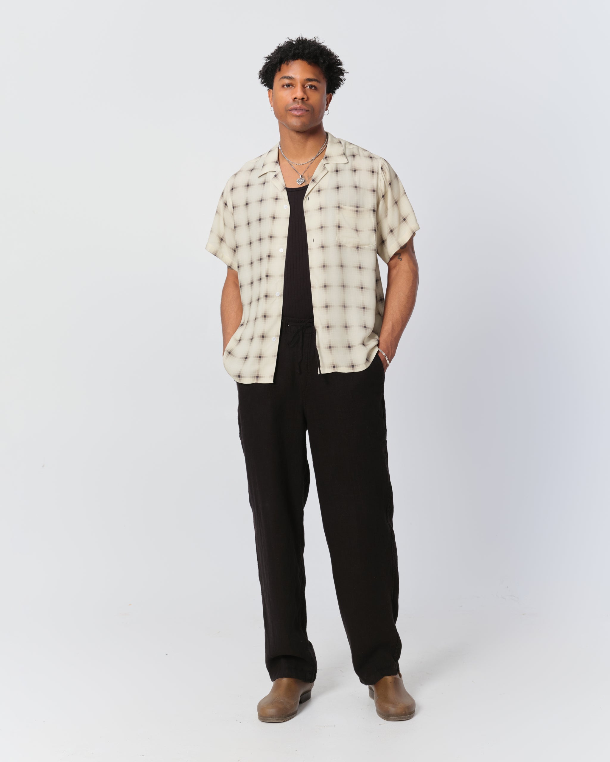 Male model wearing a white patterned camp shirt and black pants 