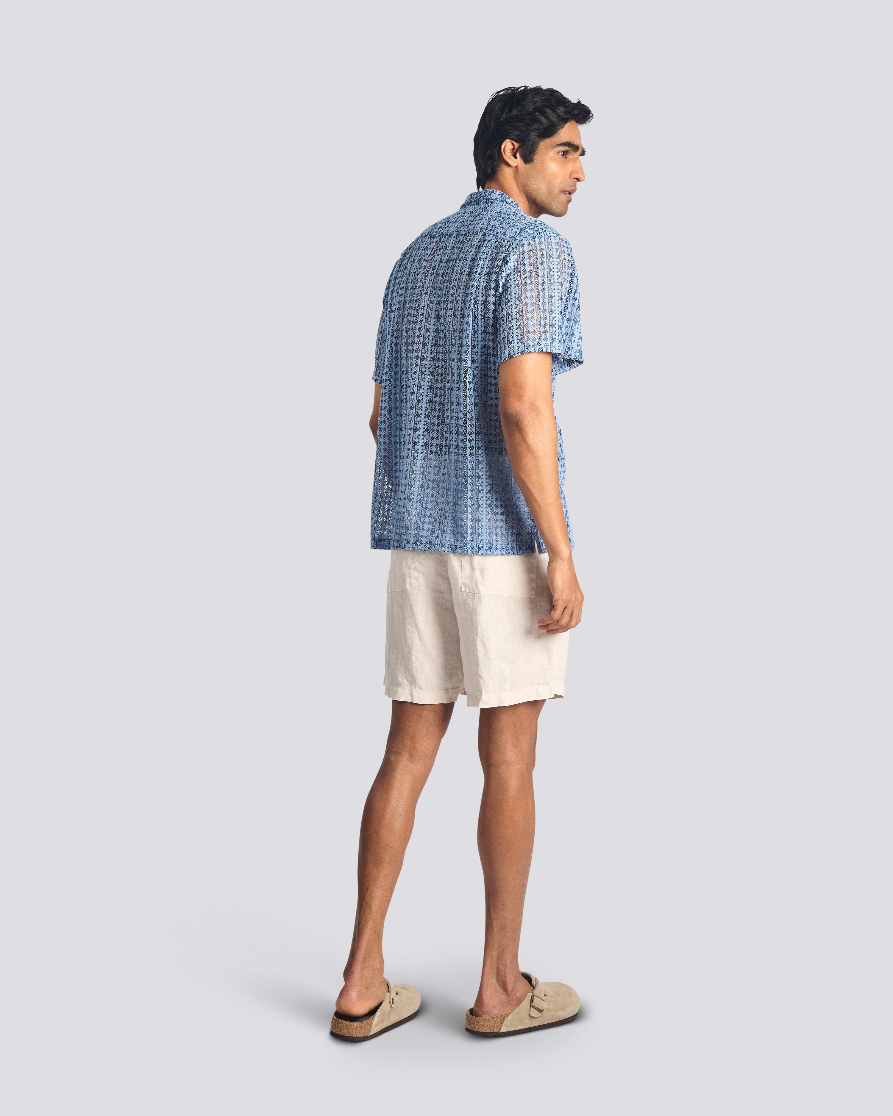 Man wearing a blue patterned shirt and beige shorts on a light gray background