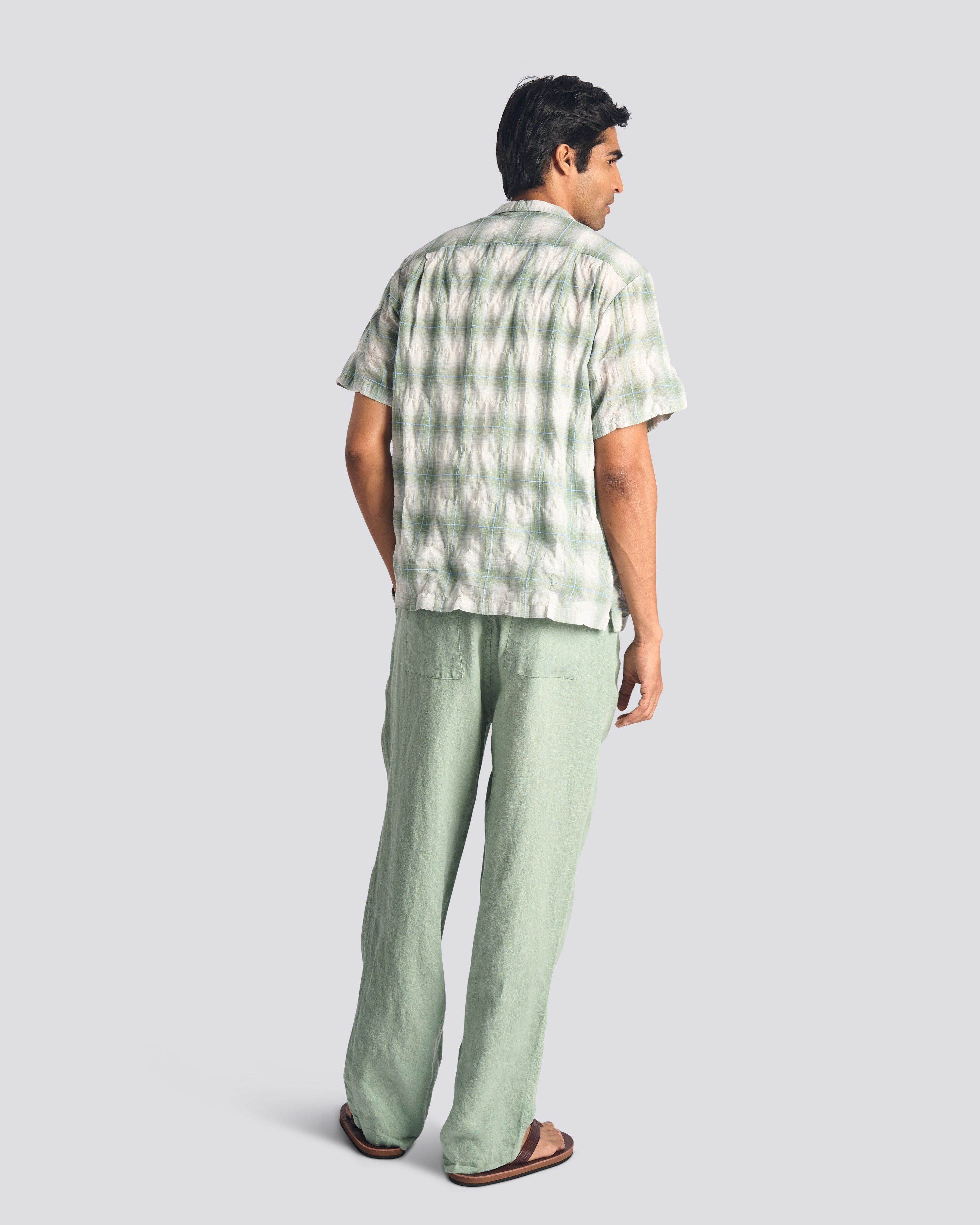 Man wearing a green checkered shirt and pants on a light gray background