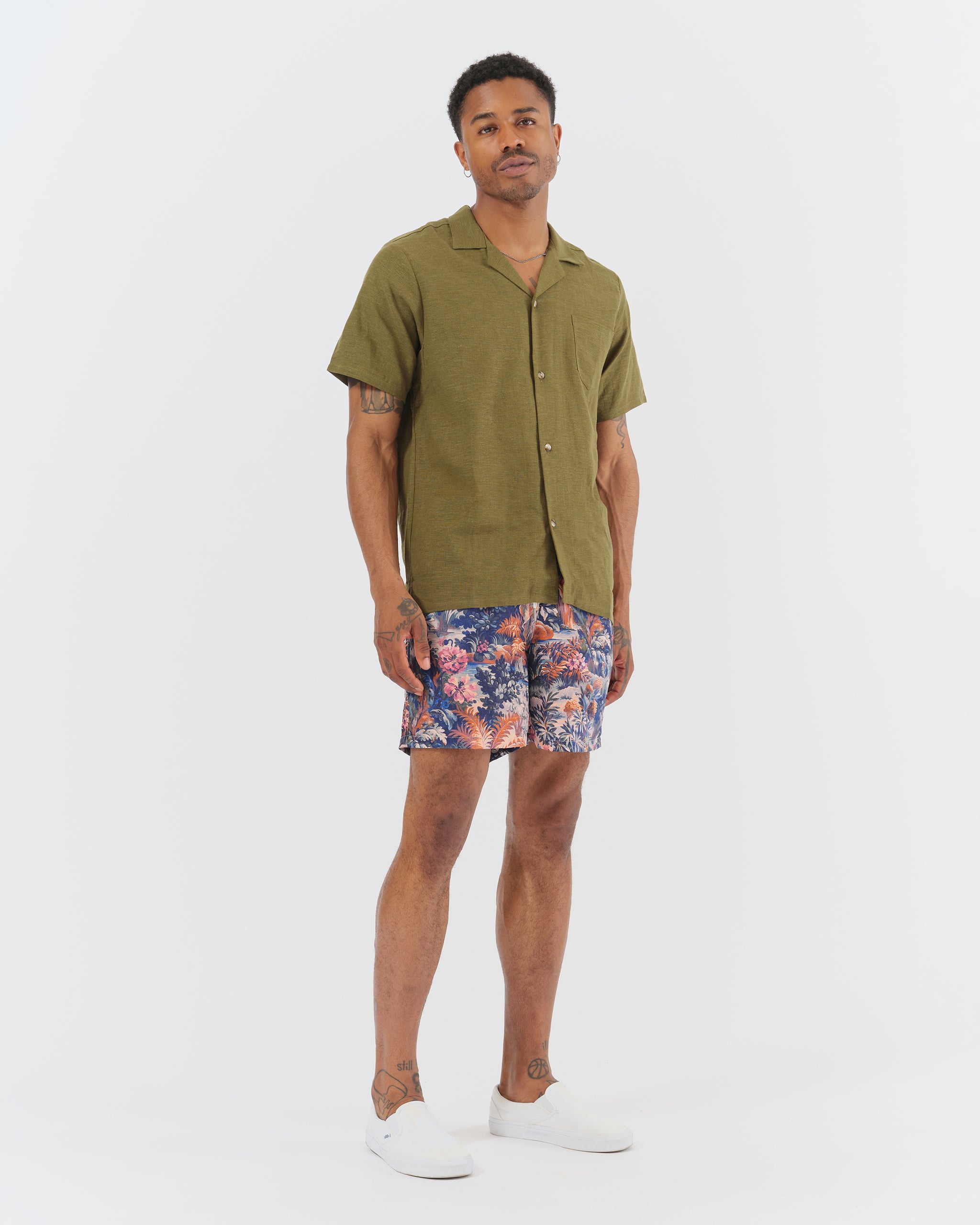 An olive green linen camp shirt with a chest pocket and two lower pockets on the front on model
