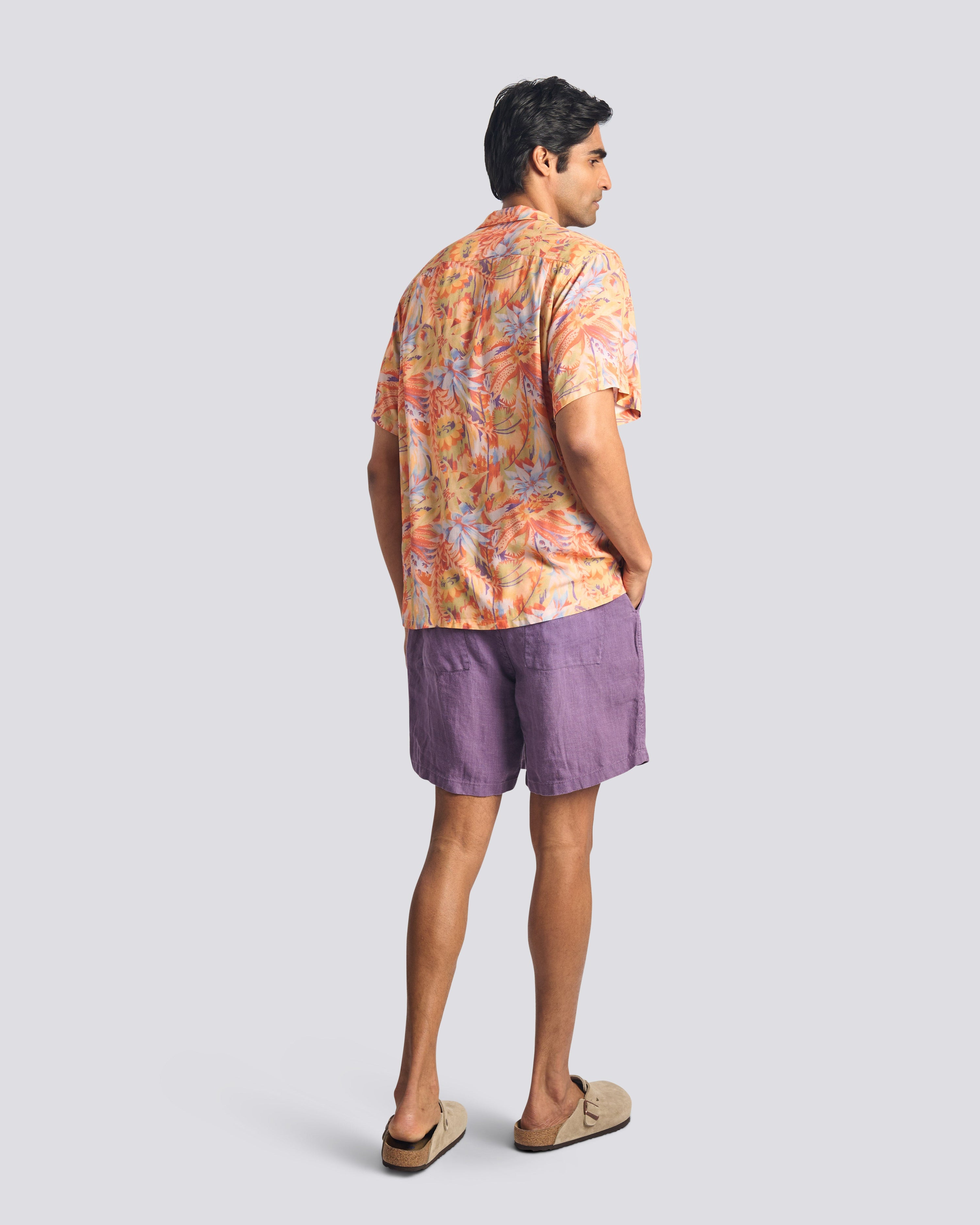 Man wearing a colorful floral shirt and purple shorts on a light gray background