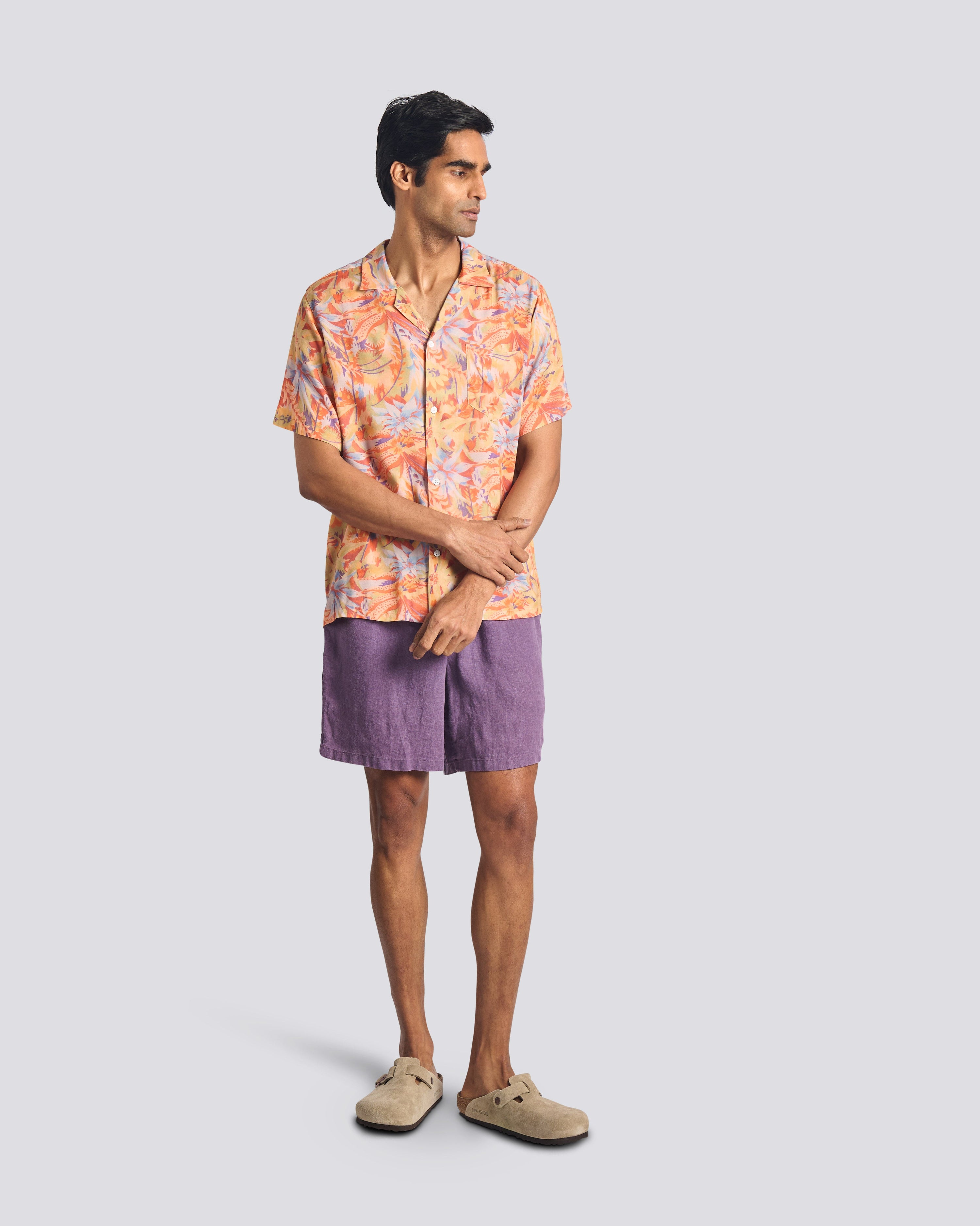 Man wearing a patterned shirt and purple shorts on a light gray background